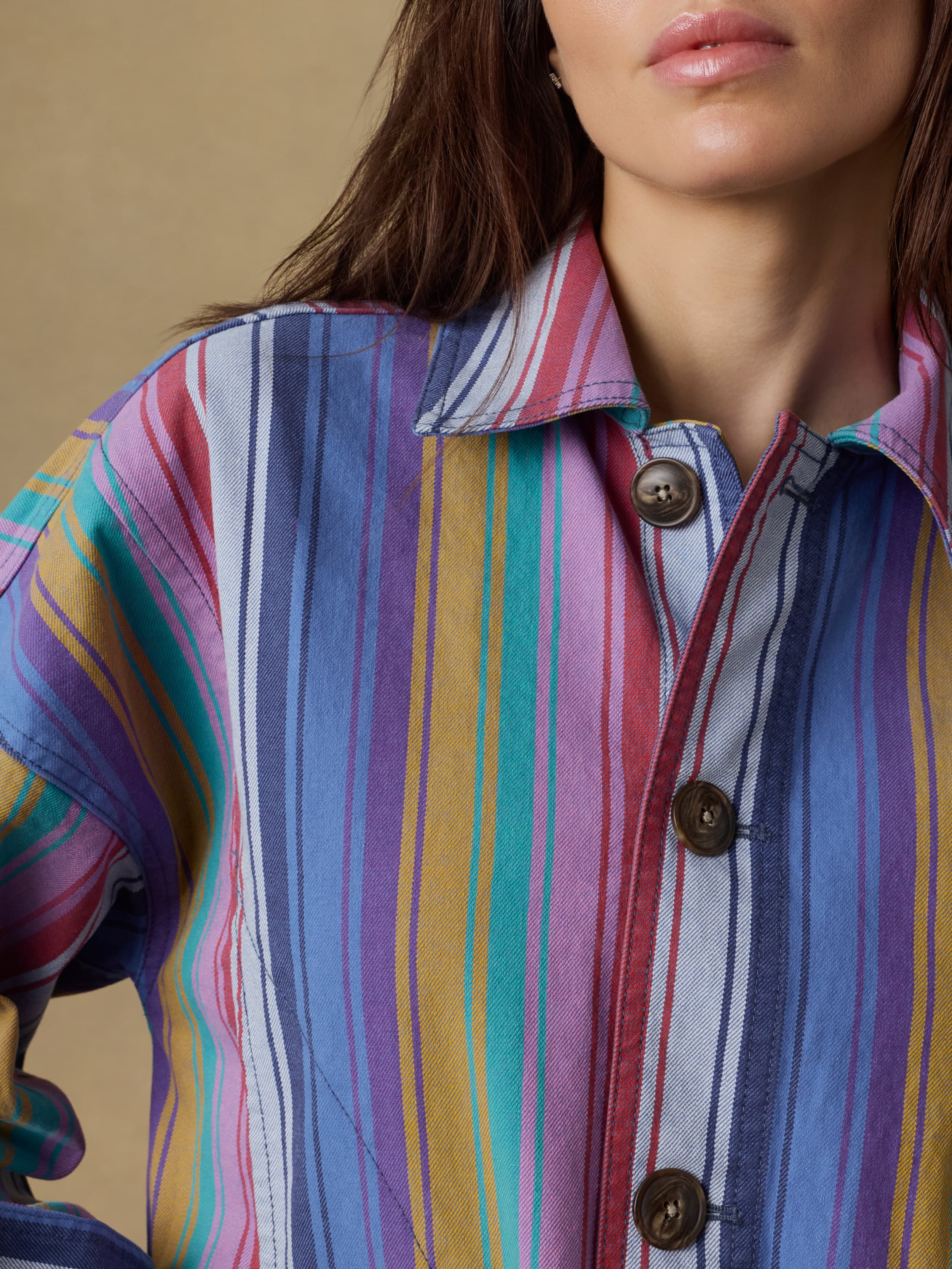 Close-up of a woman wearing a colorful striped jacket against a beige background
