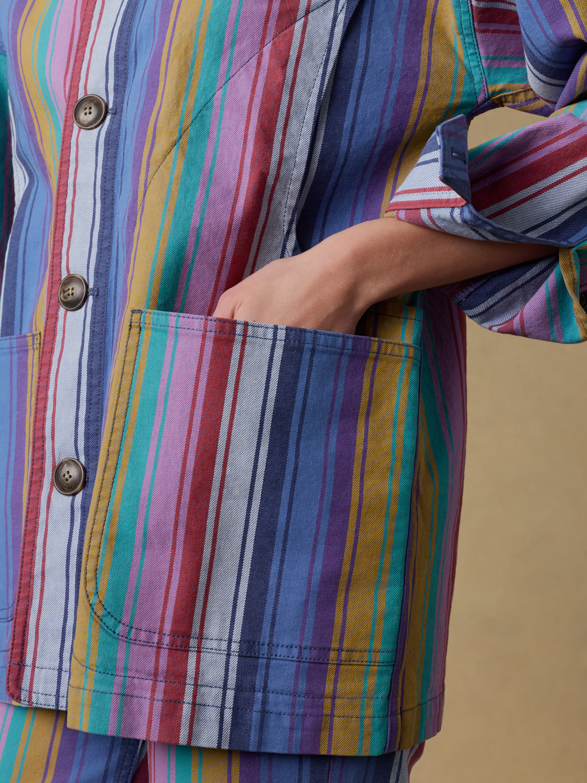 Close up of a woman wearing a multicolored striped jacket with a pocket on a beige background