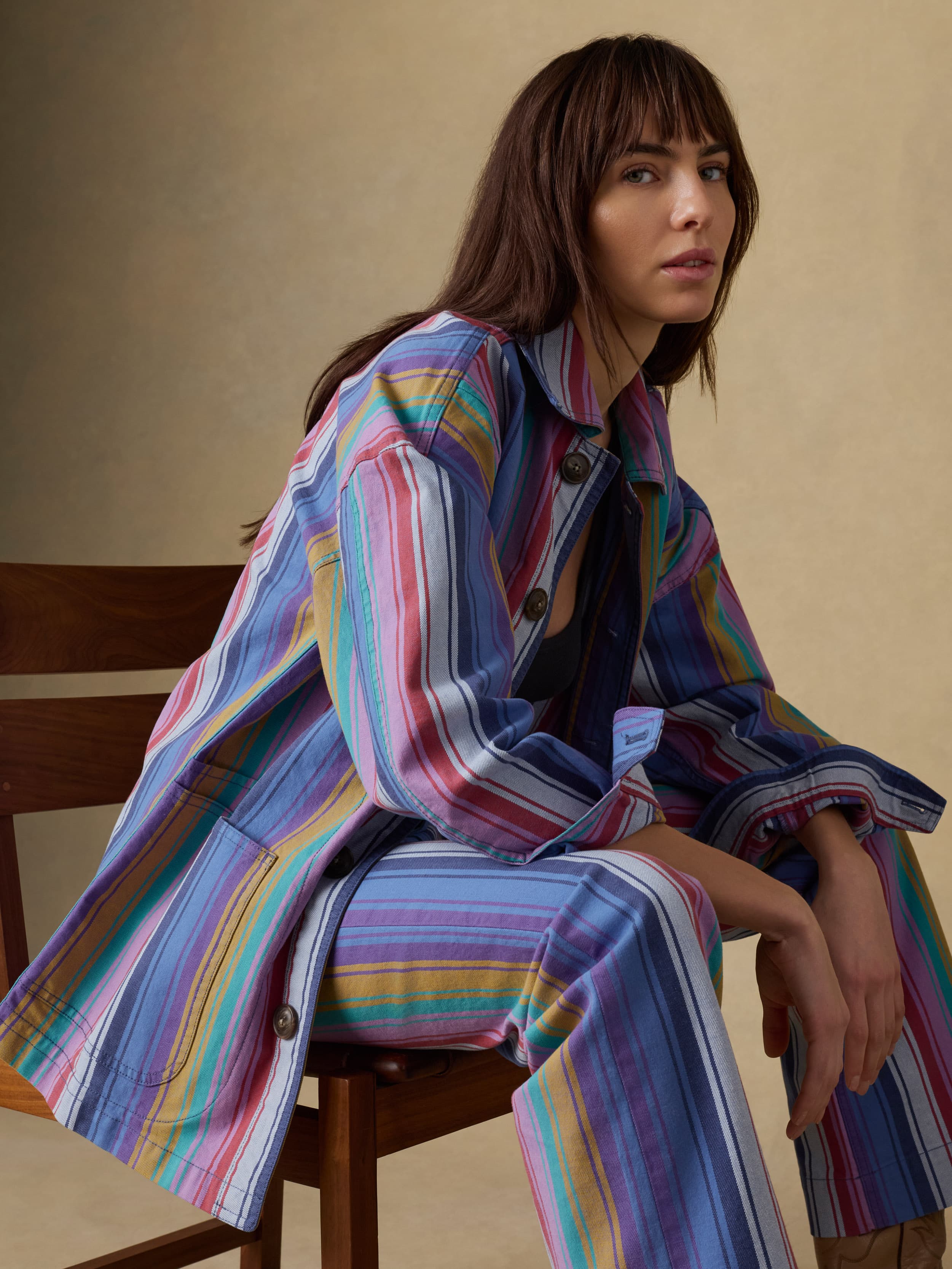 Woman wearing a colorful striped outfit sitting on a chair against a beige background