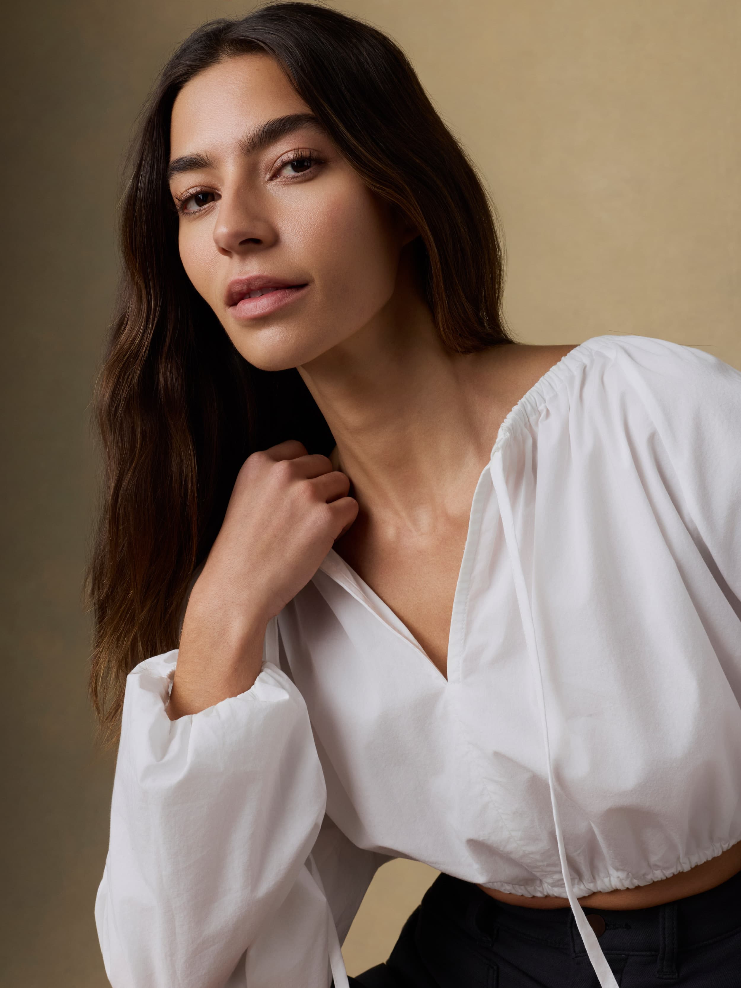 Close up of a woman wearing a white blouse against a beige background