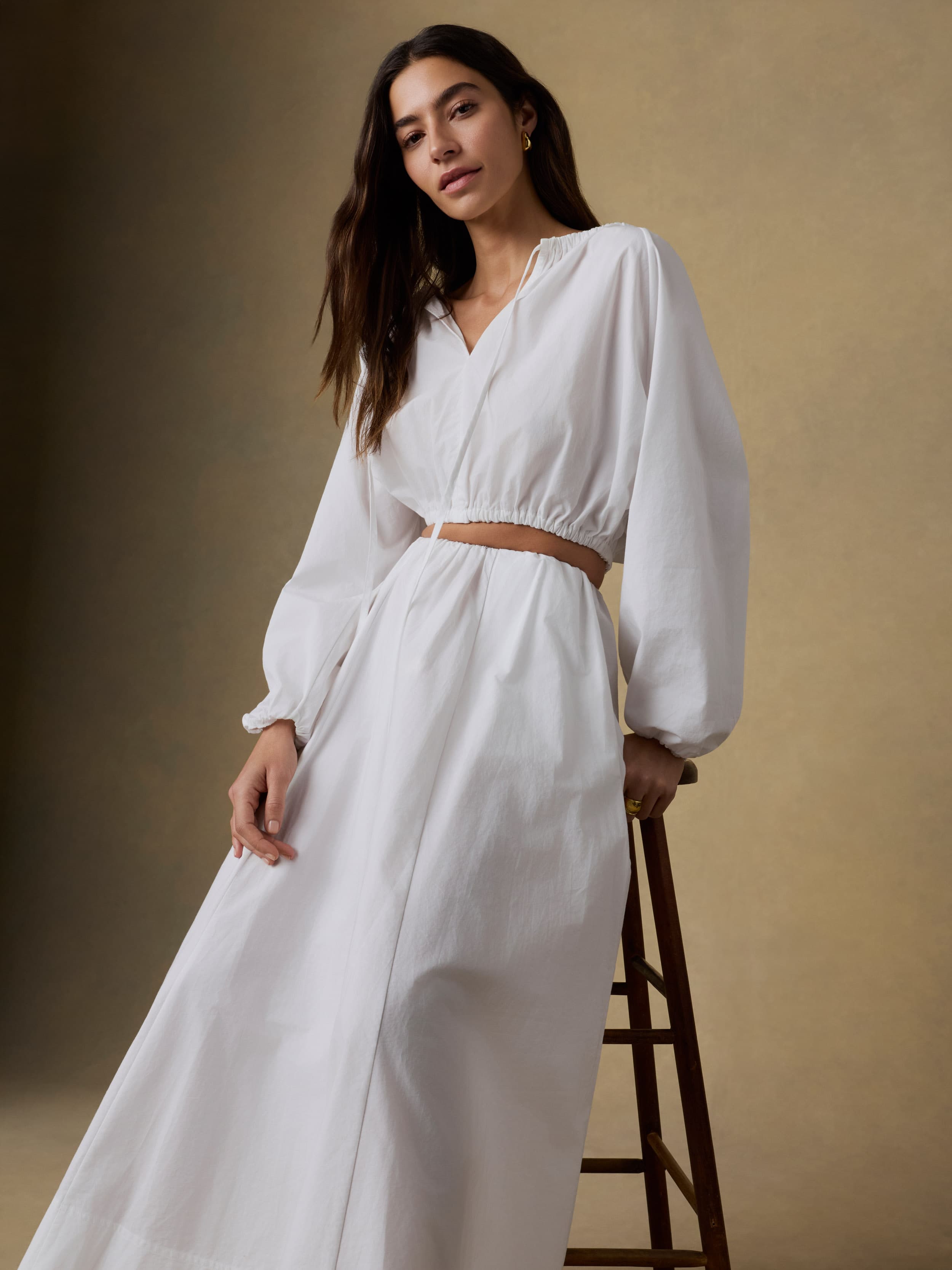 Woman wearing a white crop top and matching shirt with long sleeves against a beige background