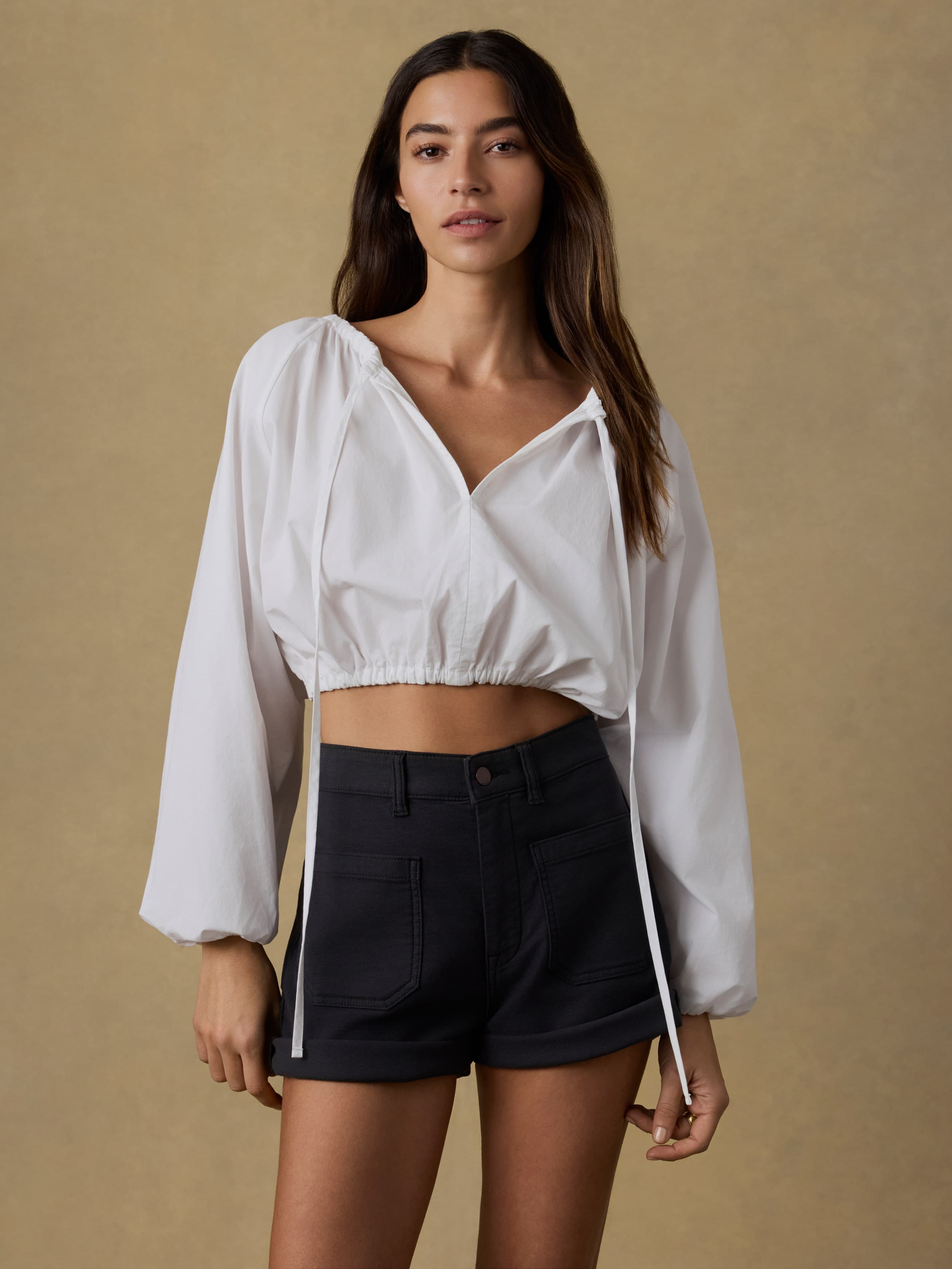 Woman wearing a white blouse and black shorts against a beige background