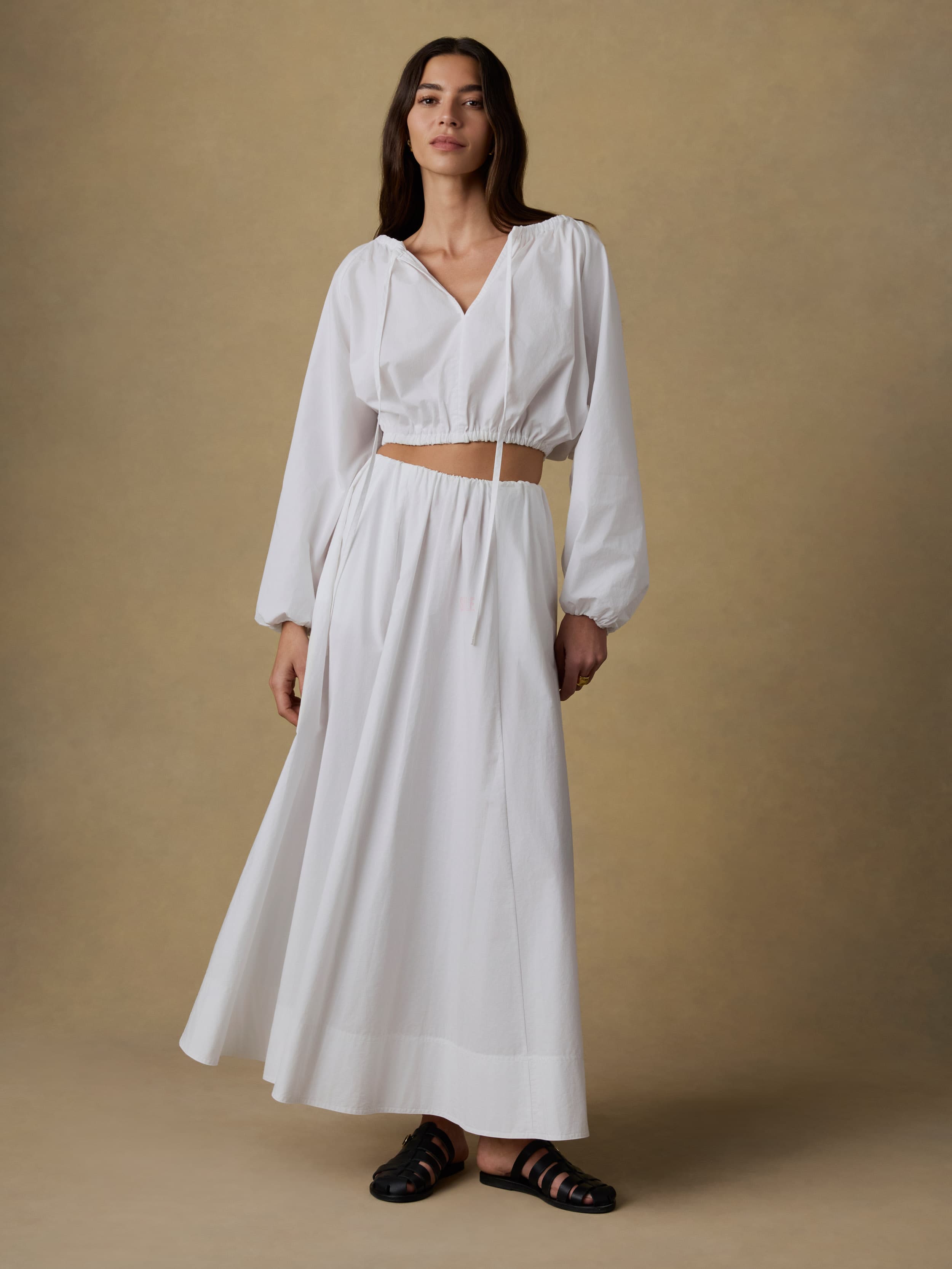 Woman wearing a white crop top and matching skirt against a beige background