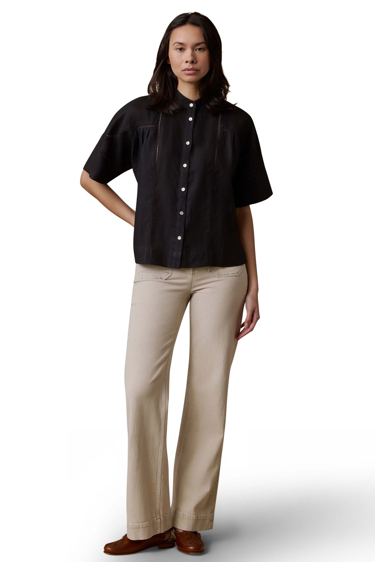 A woman wearing a black shirt, beige pants, and brown shoes, image 2 of 3
