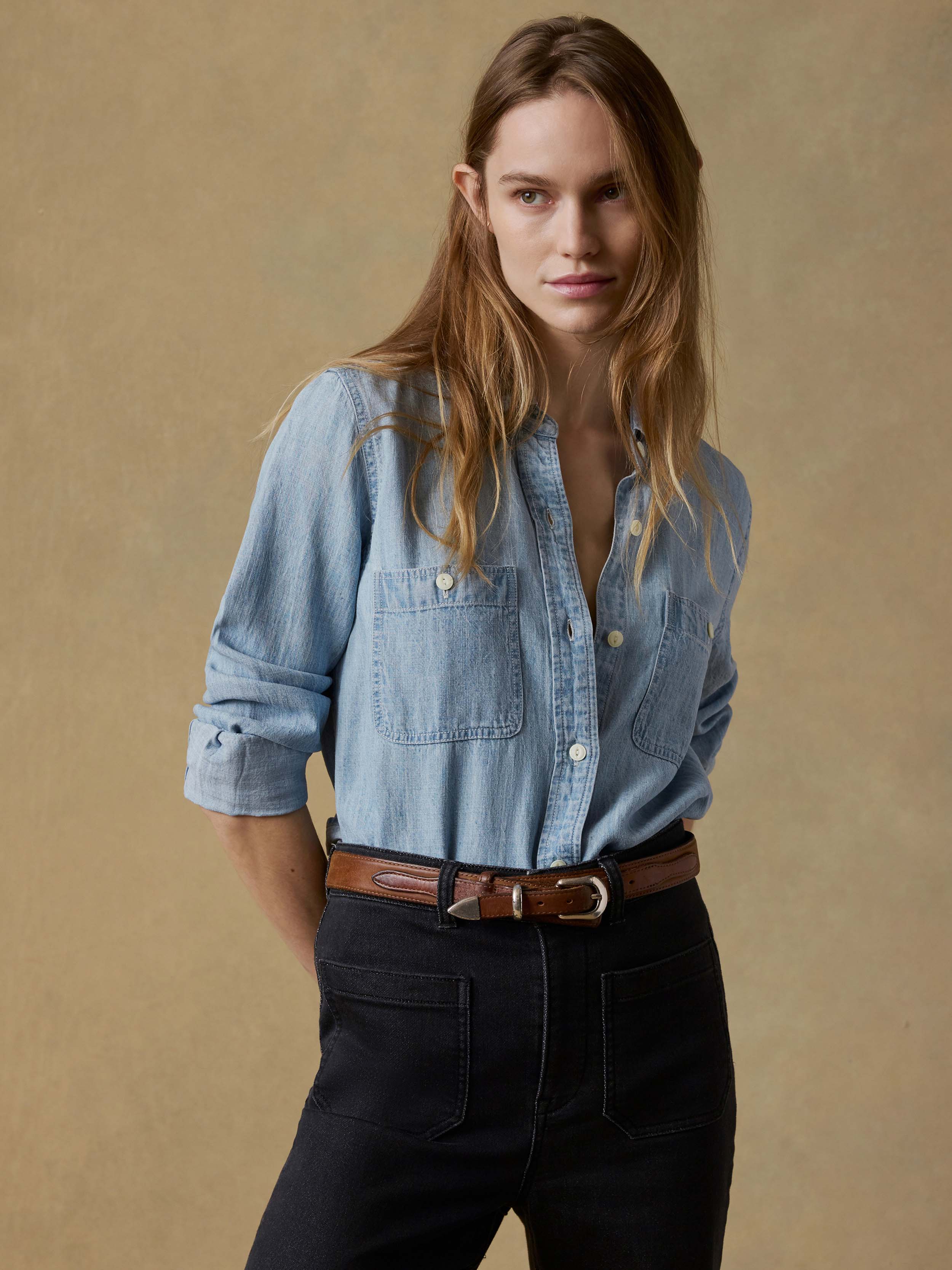Woman wearing a light blue shirt and black jeans against a beige background