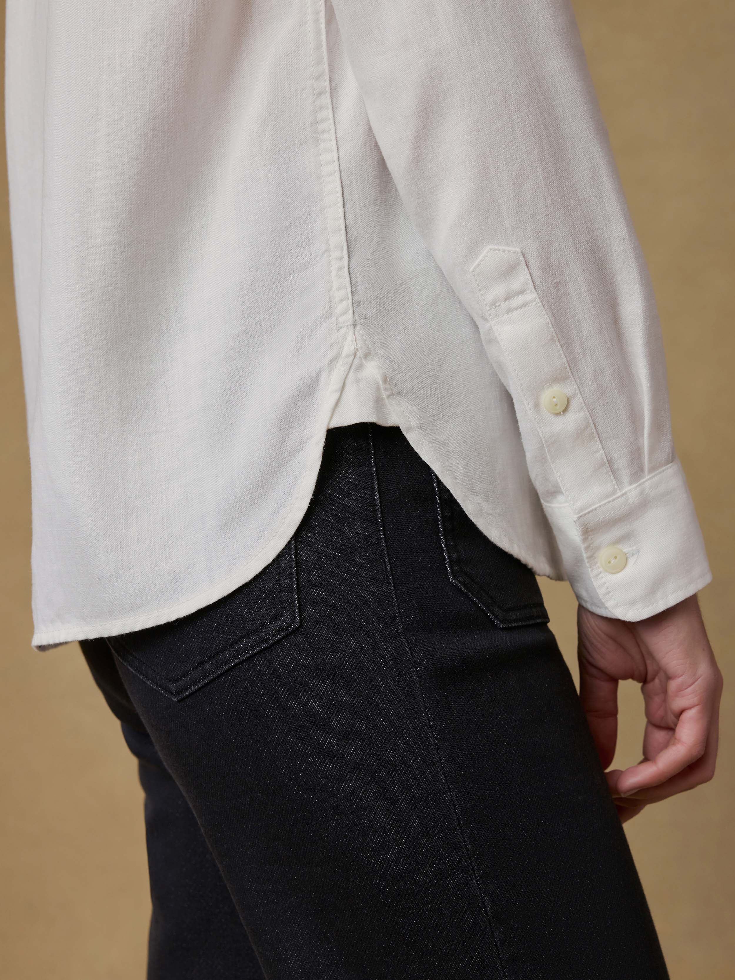 Detail shot of a woman wearing a white chambray shirt with black jeans against a beige background
