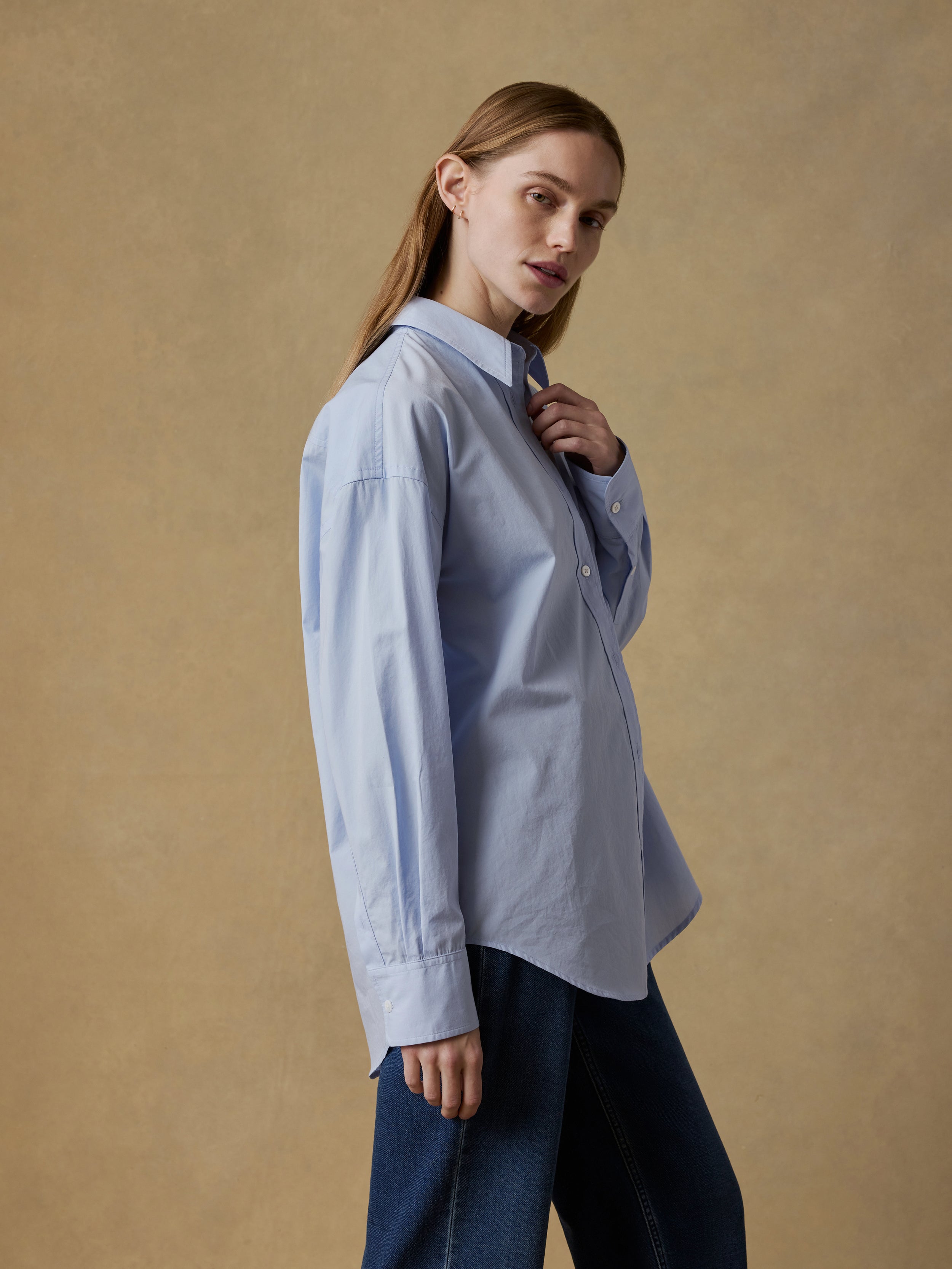 Woman wearing a light blue shirt and blue jeans against a beige background