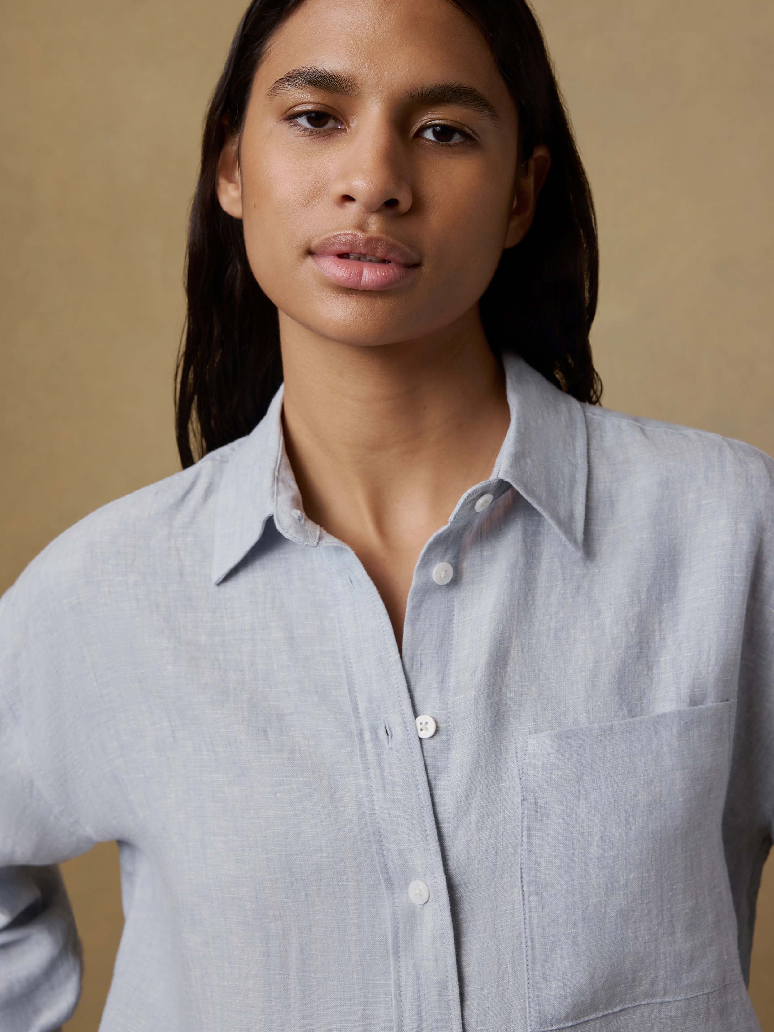 Woman wearing a light blue linen shirt against a beige background