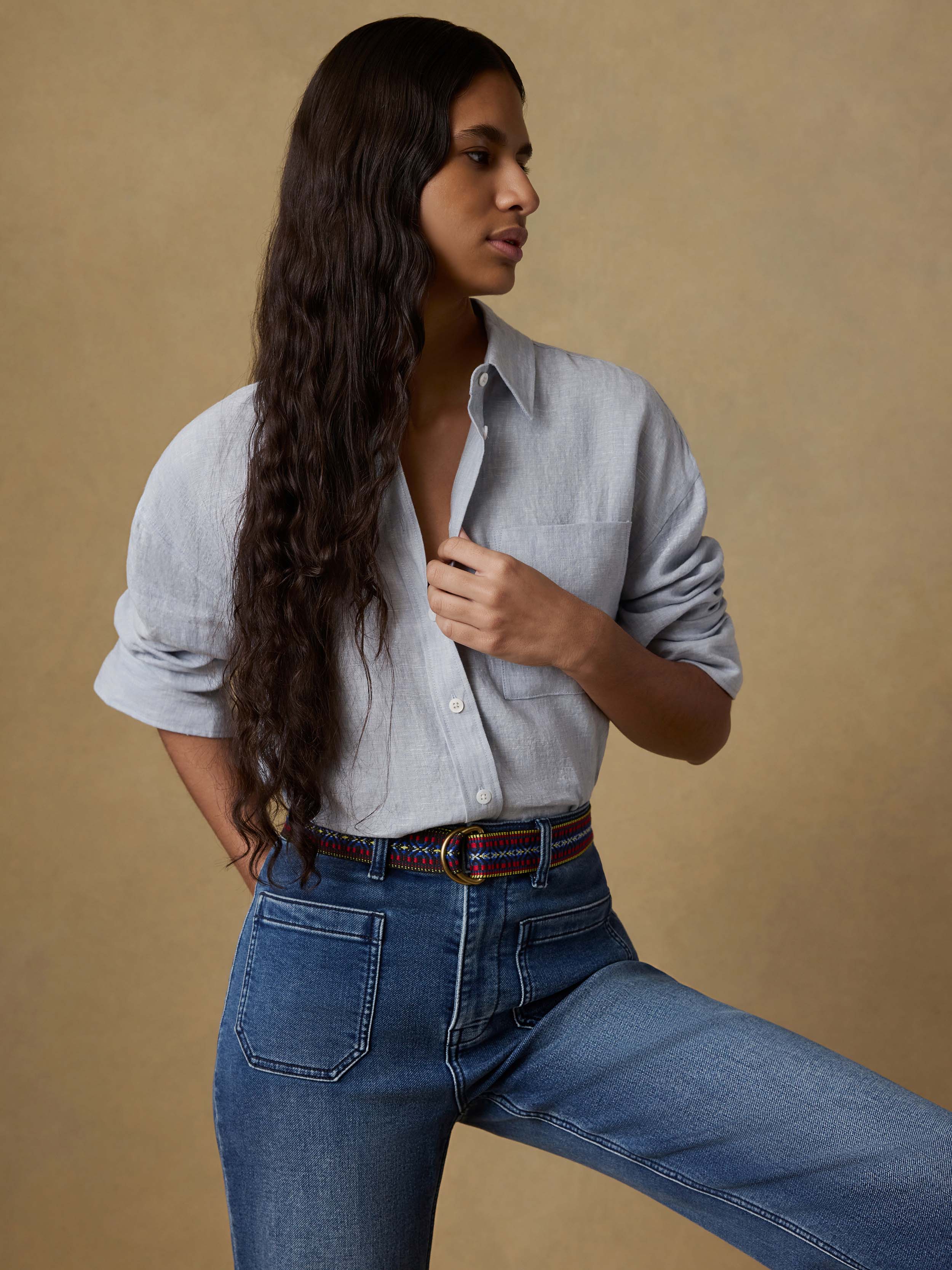 Woman wearing a light blue linen shirt and blue jeans against a beige background