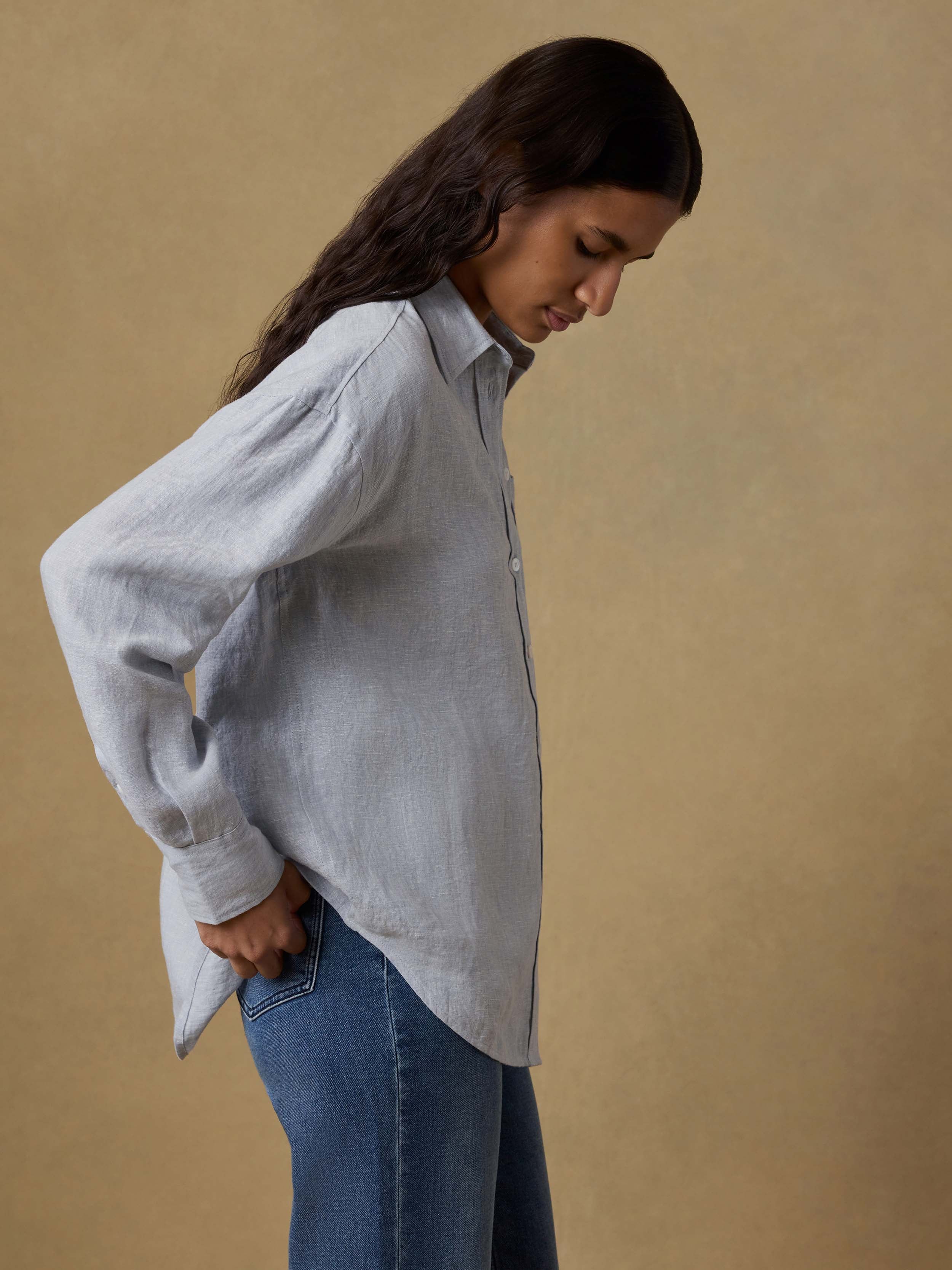 Woman wearing a light blue linen shirt and blue jeans against a beige background