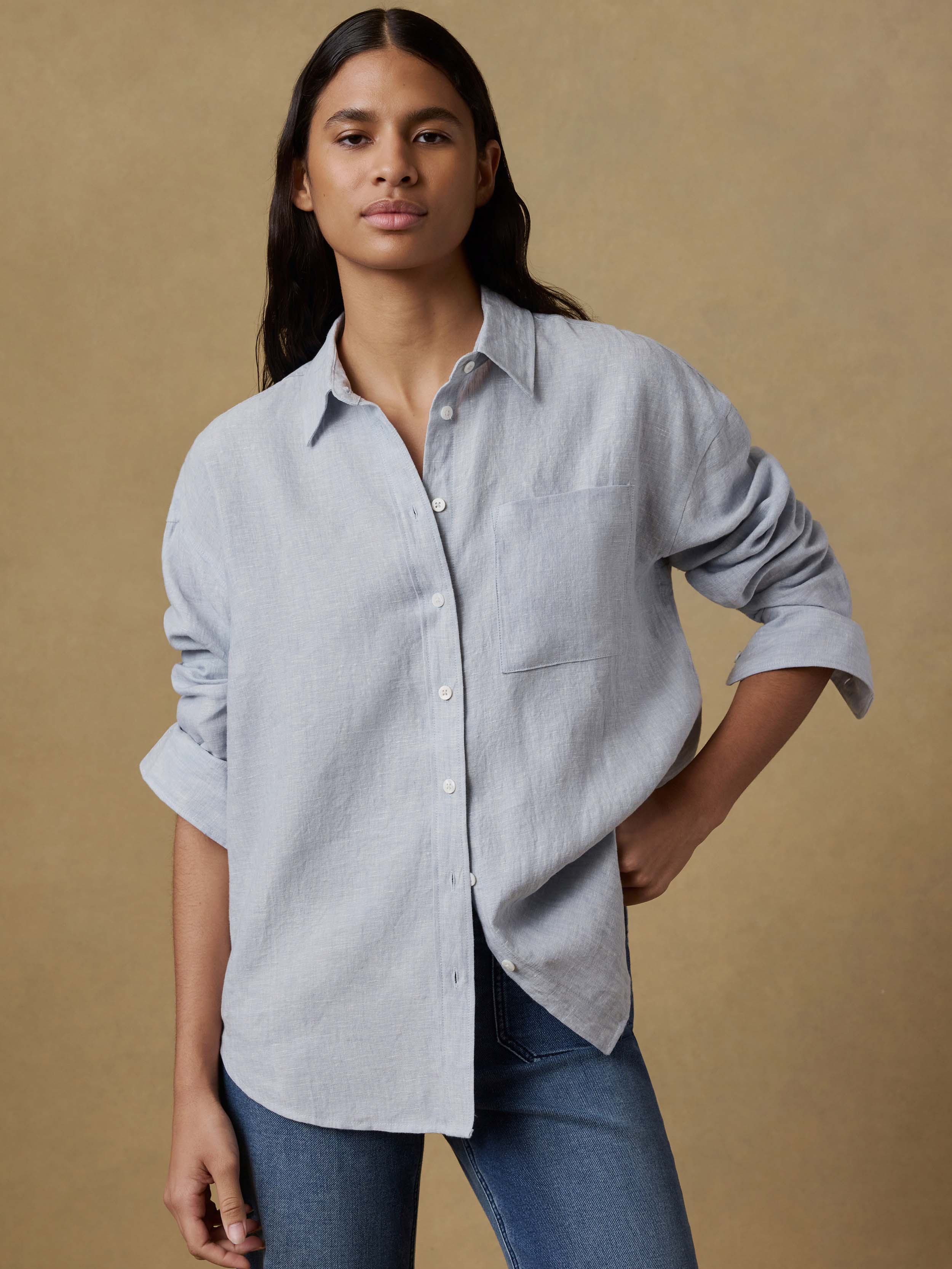 Woman wearing a light blue linen shirt and blue jeans against a beige background