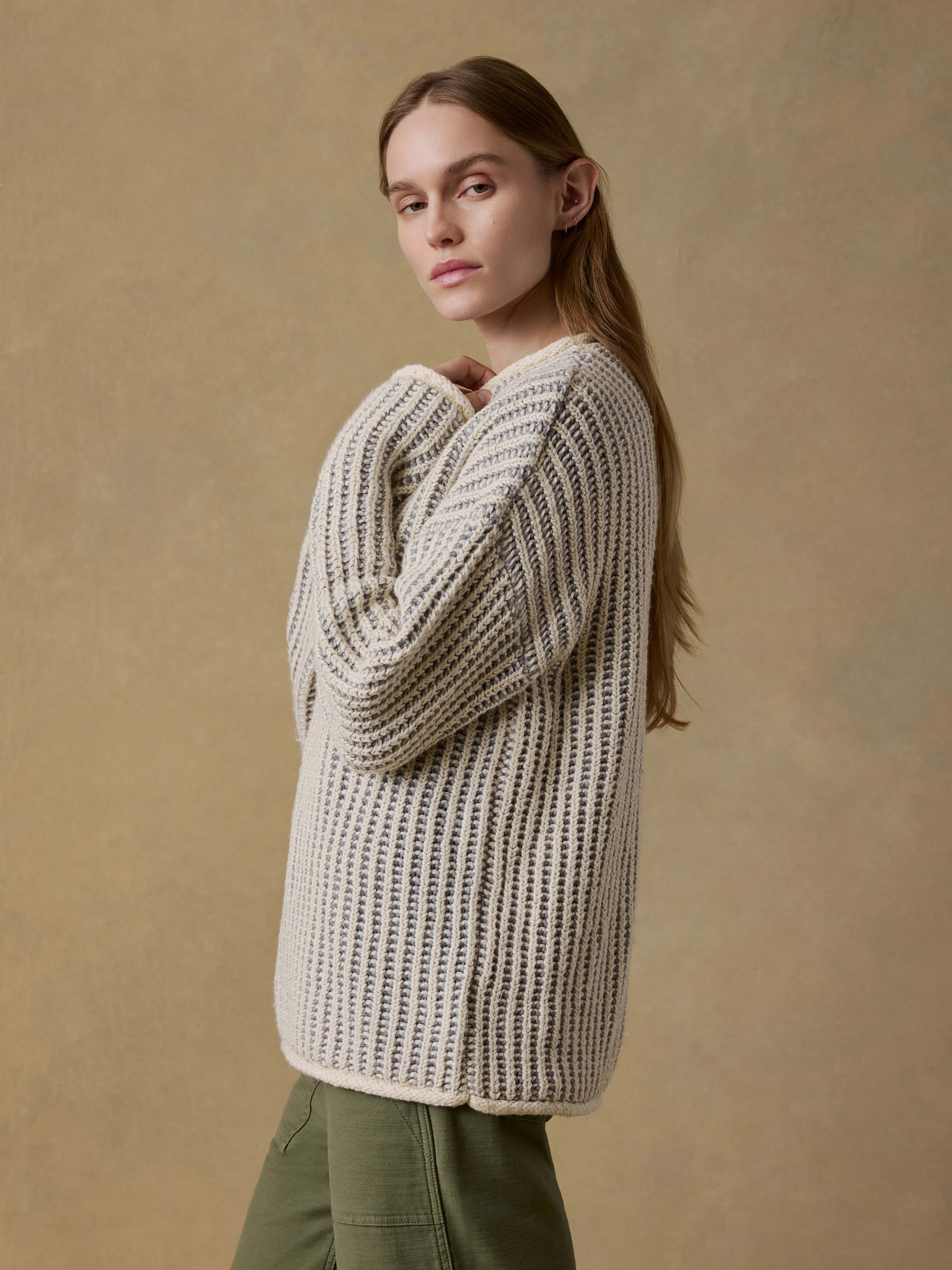 Woman wearing a chunky knit sweater and green pants against a beige background