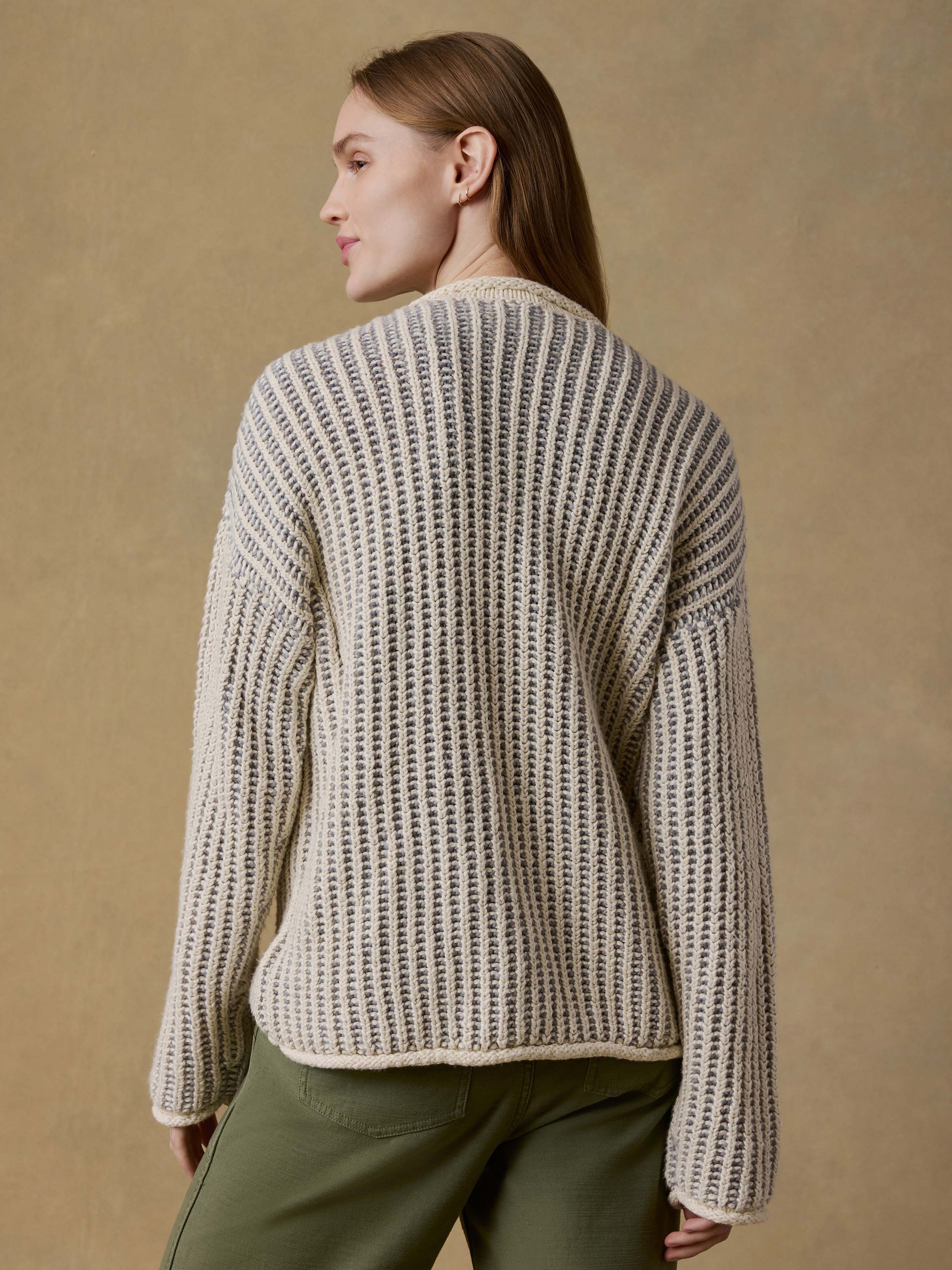 Back view of a woman wearing a chunky knit sweater and green pants against a beige background