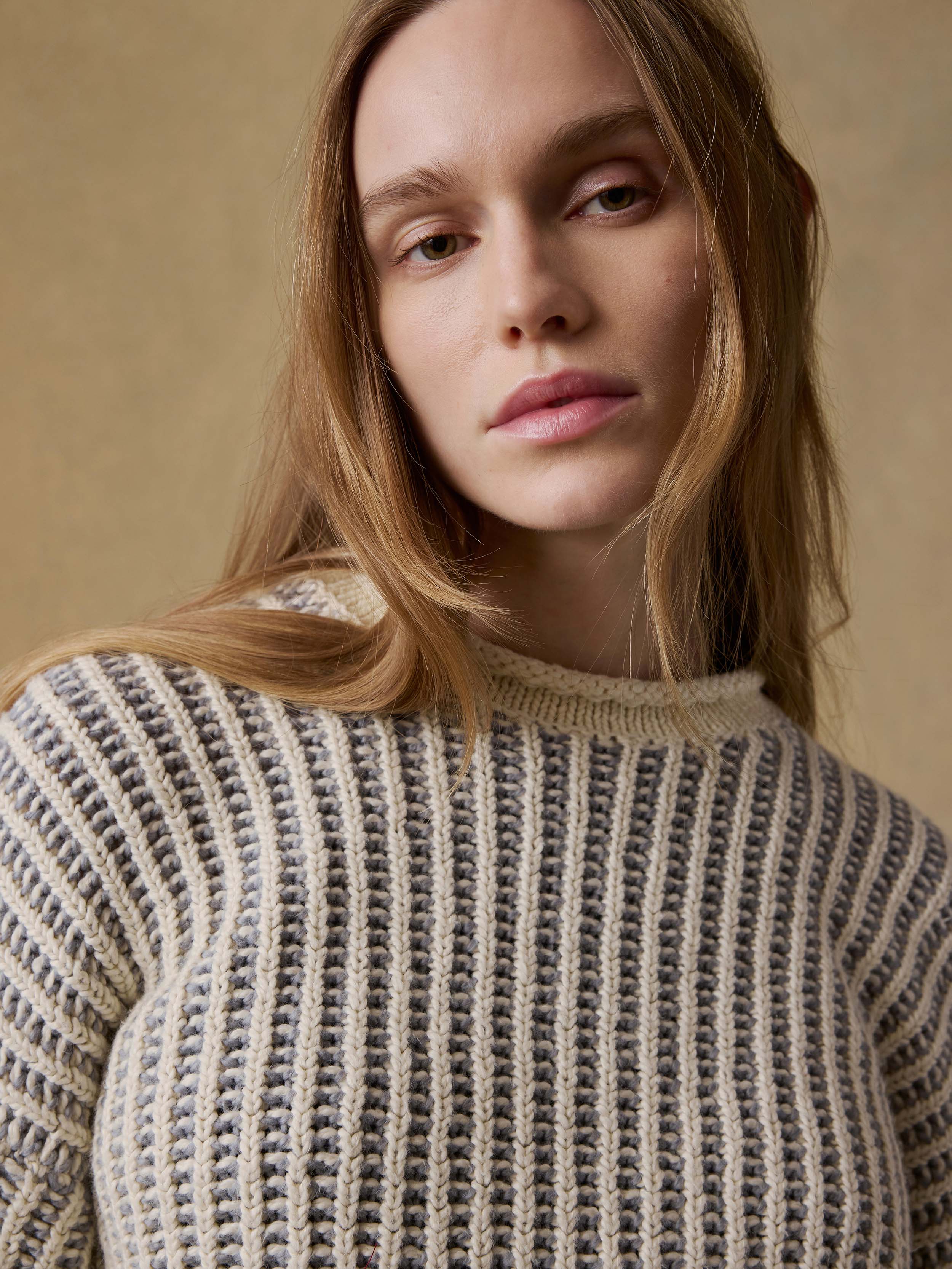 Woman wearing a chunky knit sweater against a beige background