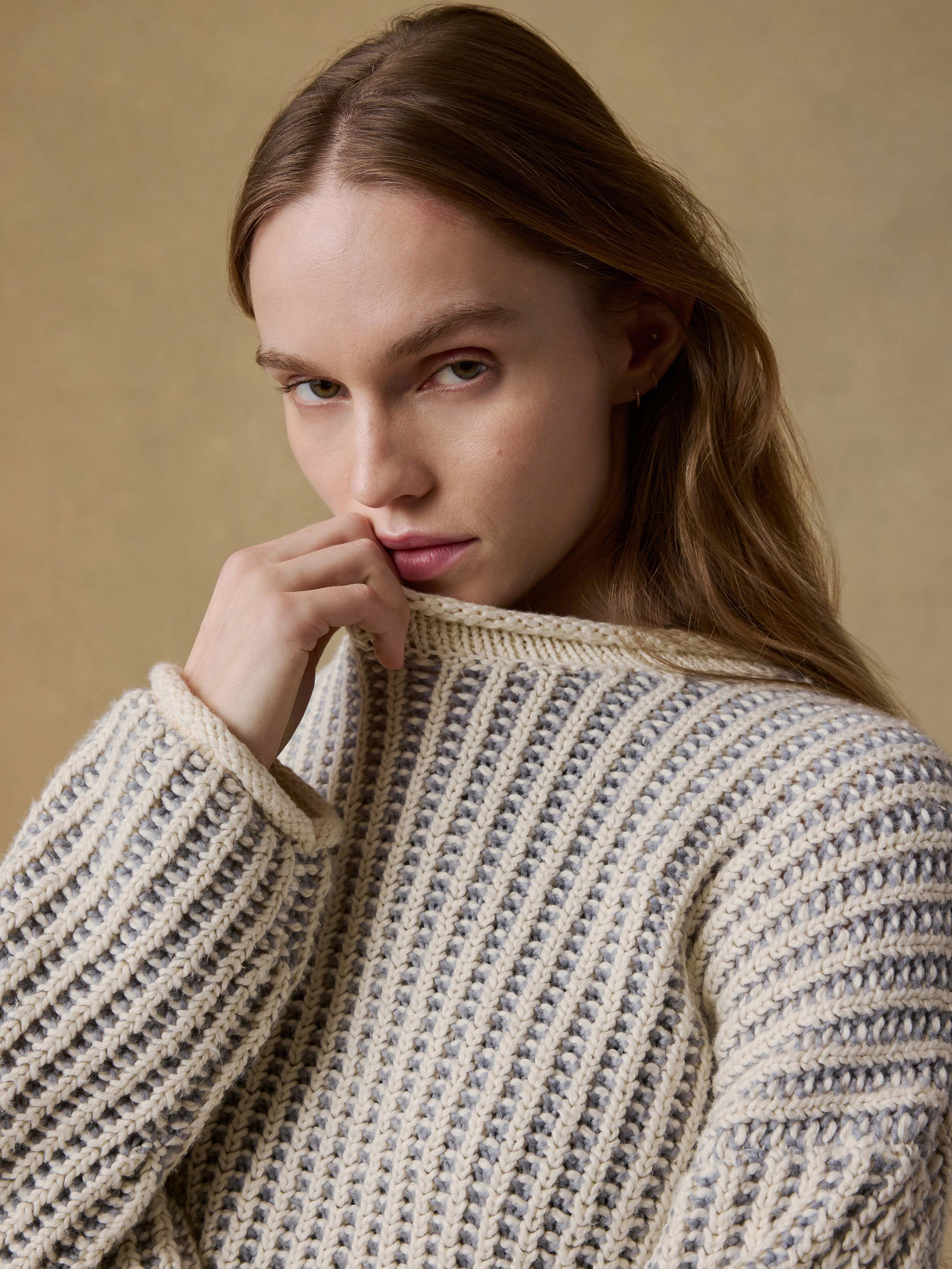 Woman wearing a chunky knit sweater against a beige background