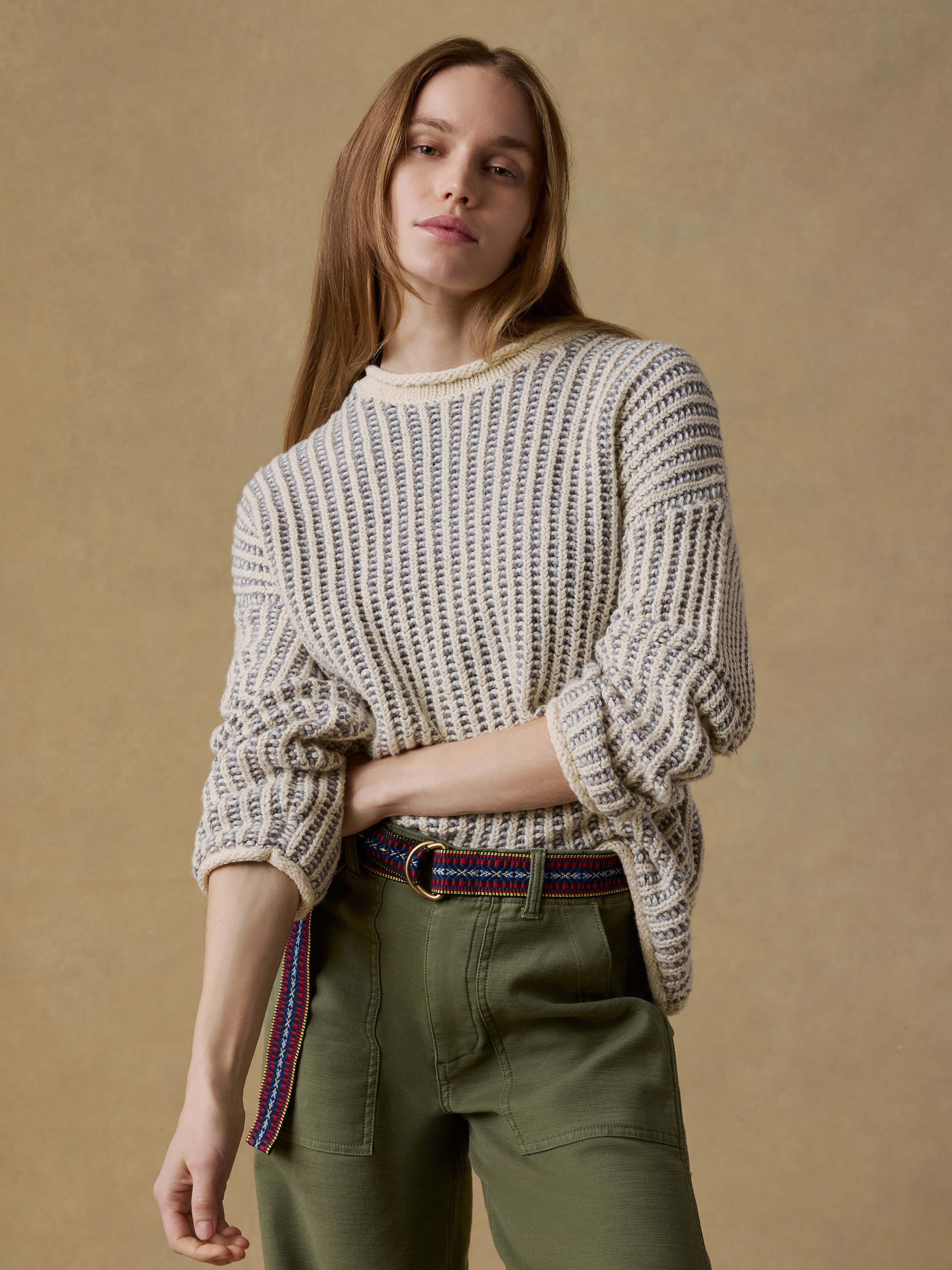 Woman wearing a chunky knit sweater and green pants against a beige background