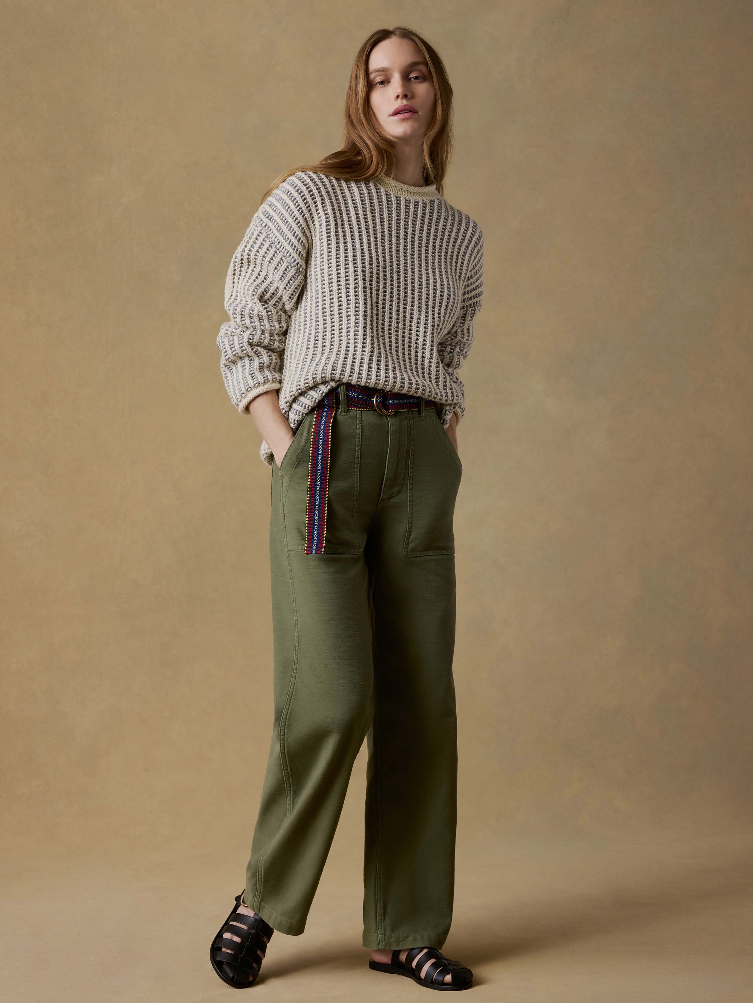 Woman wearing a chunky knit sweater and green pants against a beige background