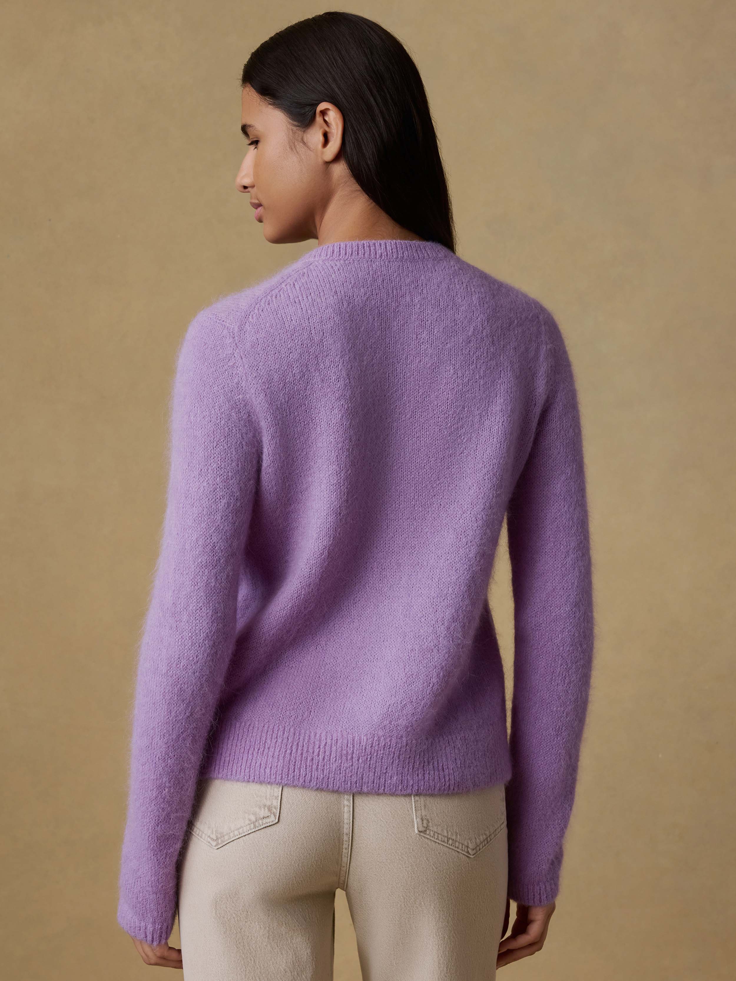 Back view of a woman wearing a purple cardigan with beige pants against a beige background