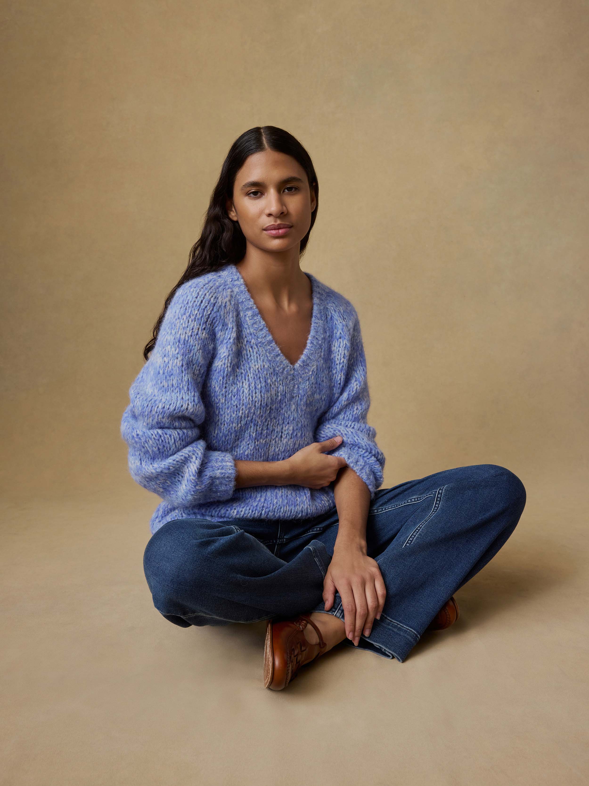 Woman wearing a blue sweater and jeans sitting on a beige background