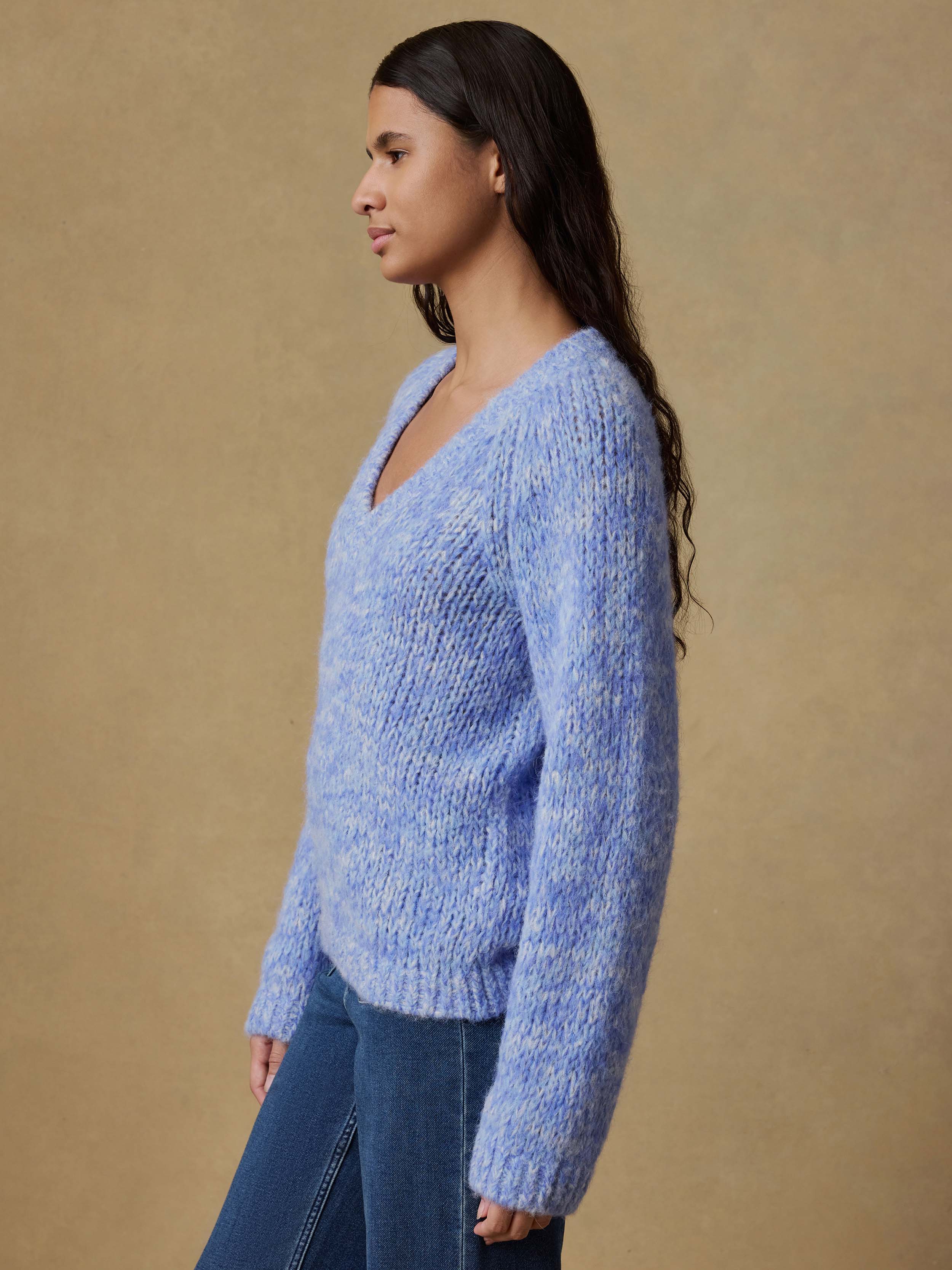 Woman wearing a blue knitted sweater and blue jeans against a beige background