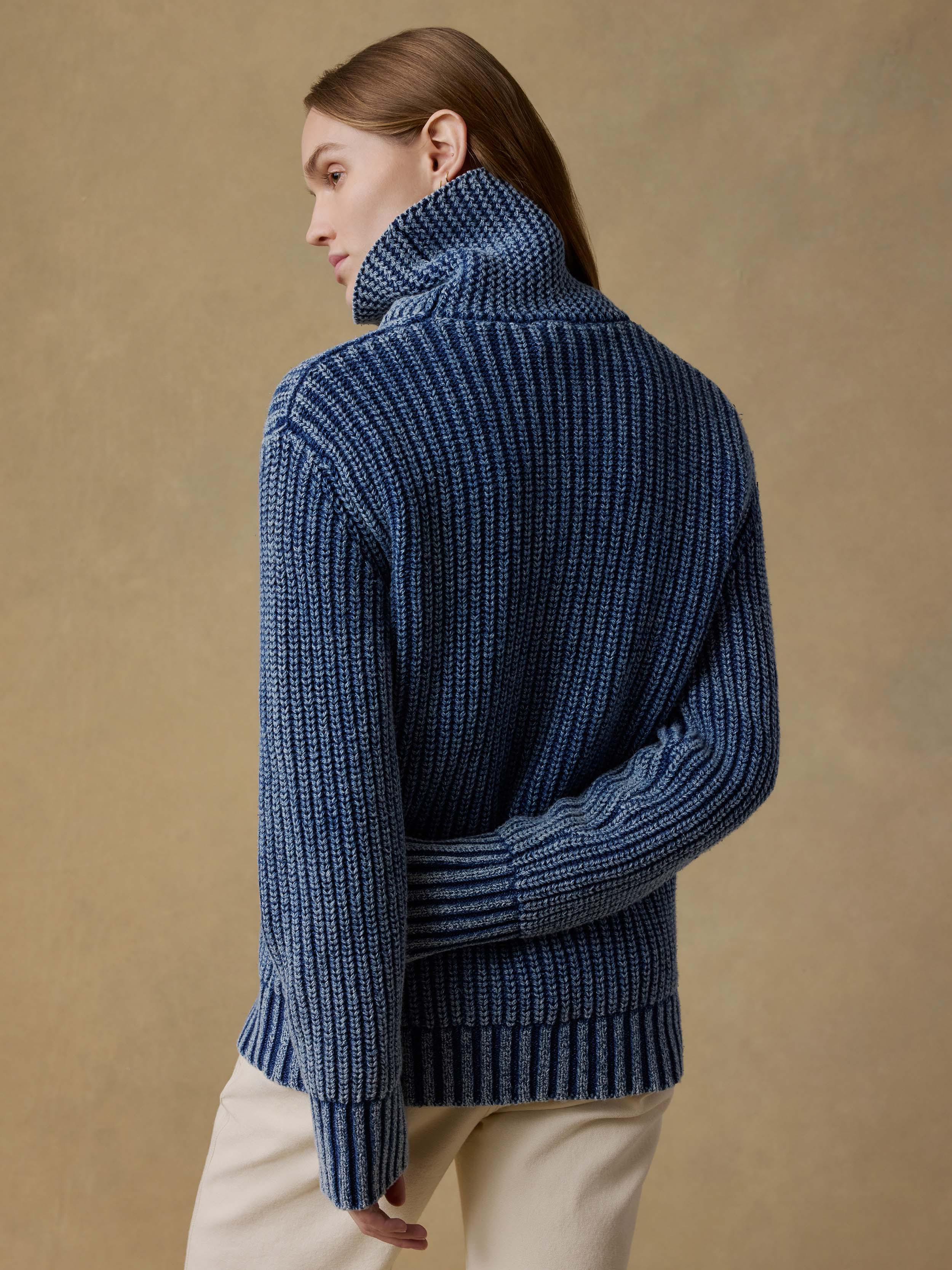 Woman wearing a blue ribbed sweater and beige pants against a beige background