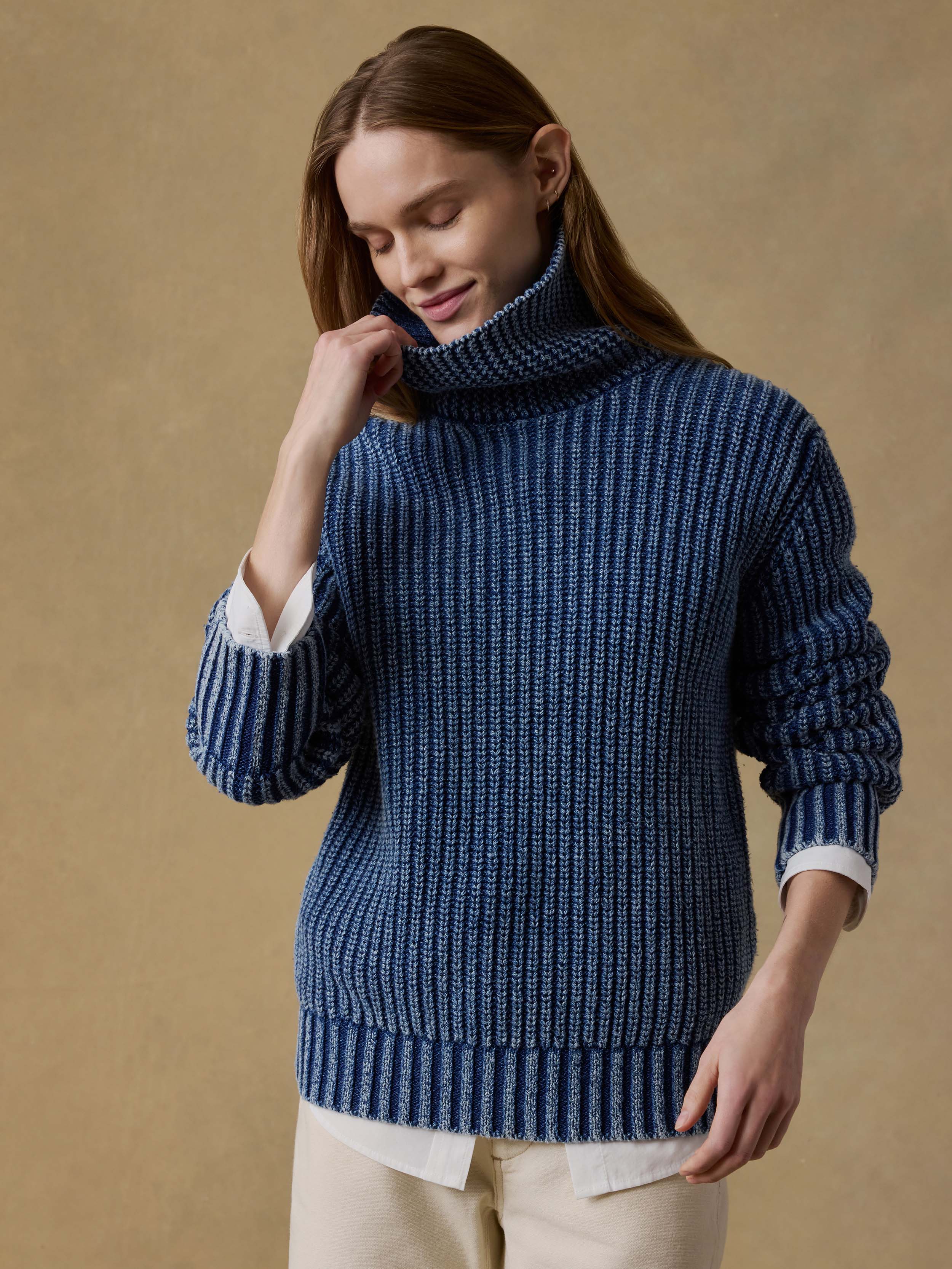 Woman wearing a blue knitted sweater and beige pants sitting on a beige background