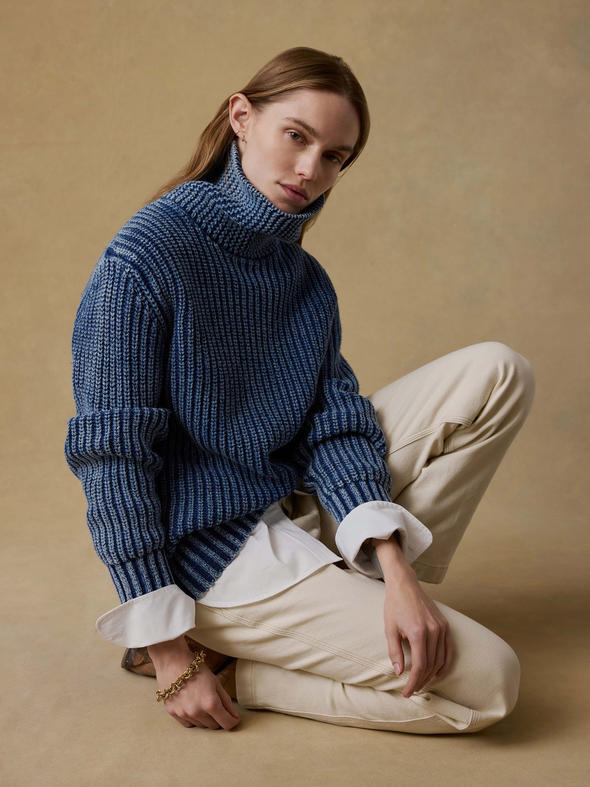 Woman wearing a blue knitted sweater and beige pants sitting on a beige background