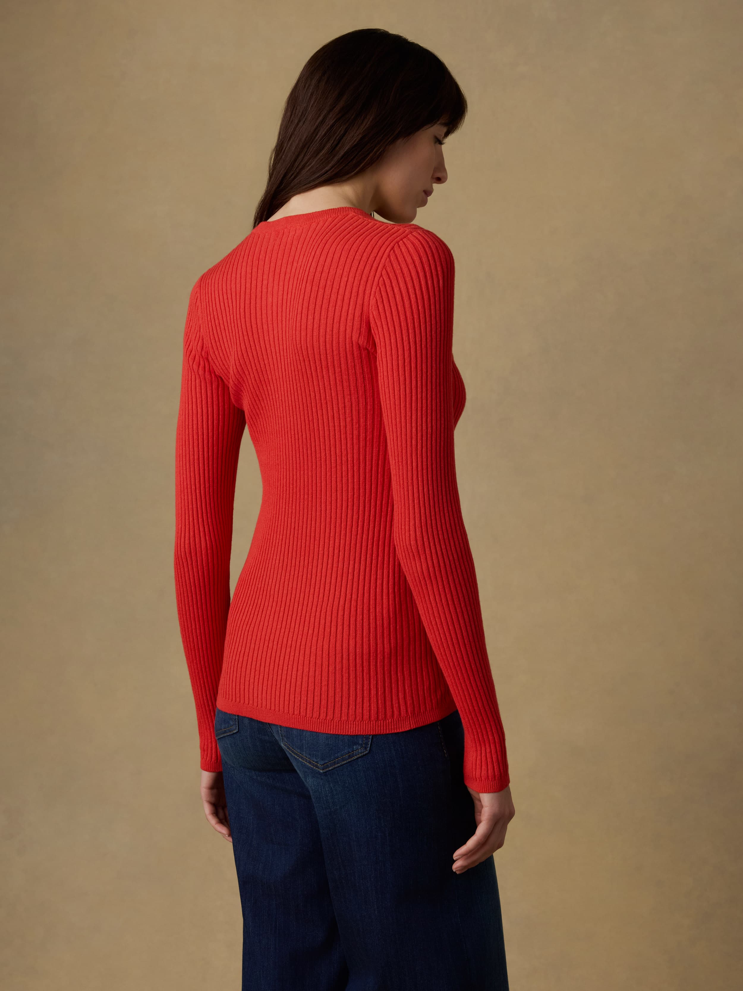 Back view of a woman wearing a red ribbed cardigan against a beige background