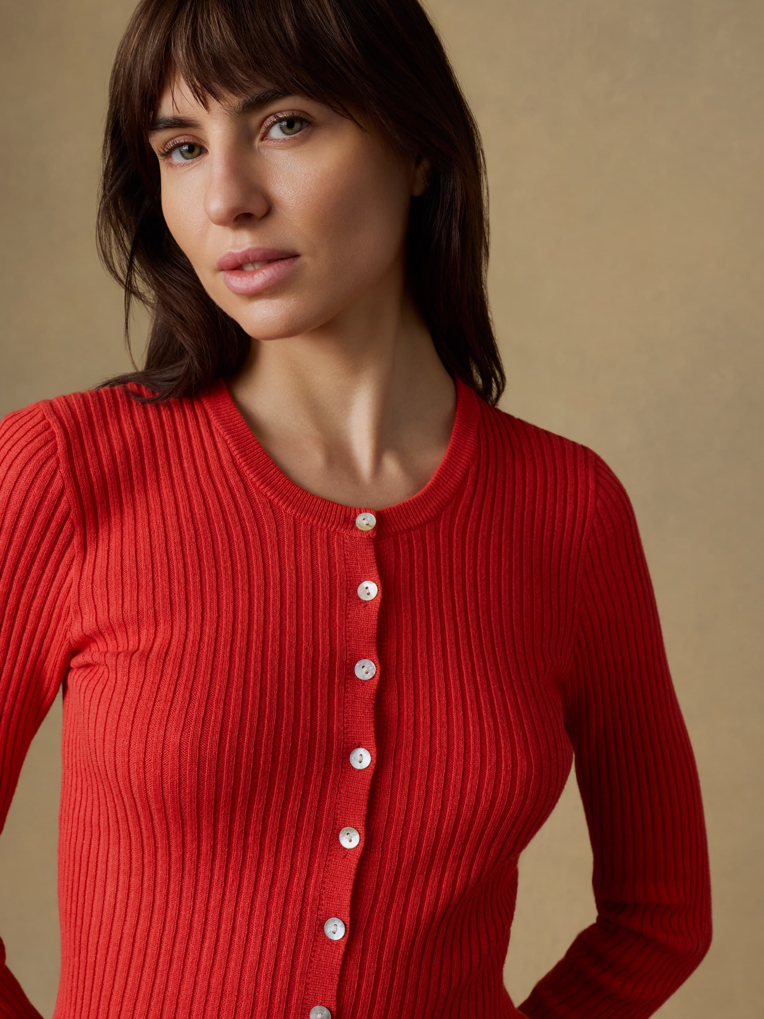 Close up of a woman wearing a red ribbed cardigan against a beige background