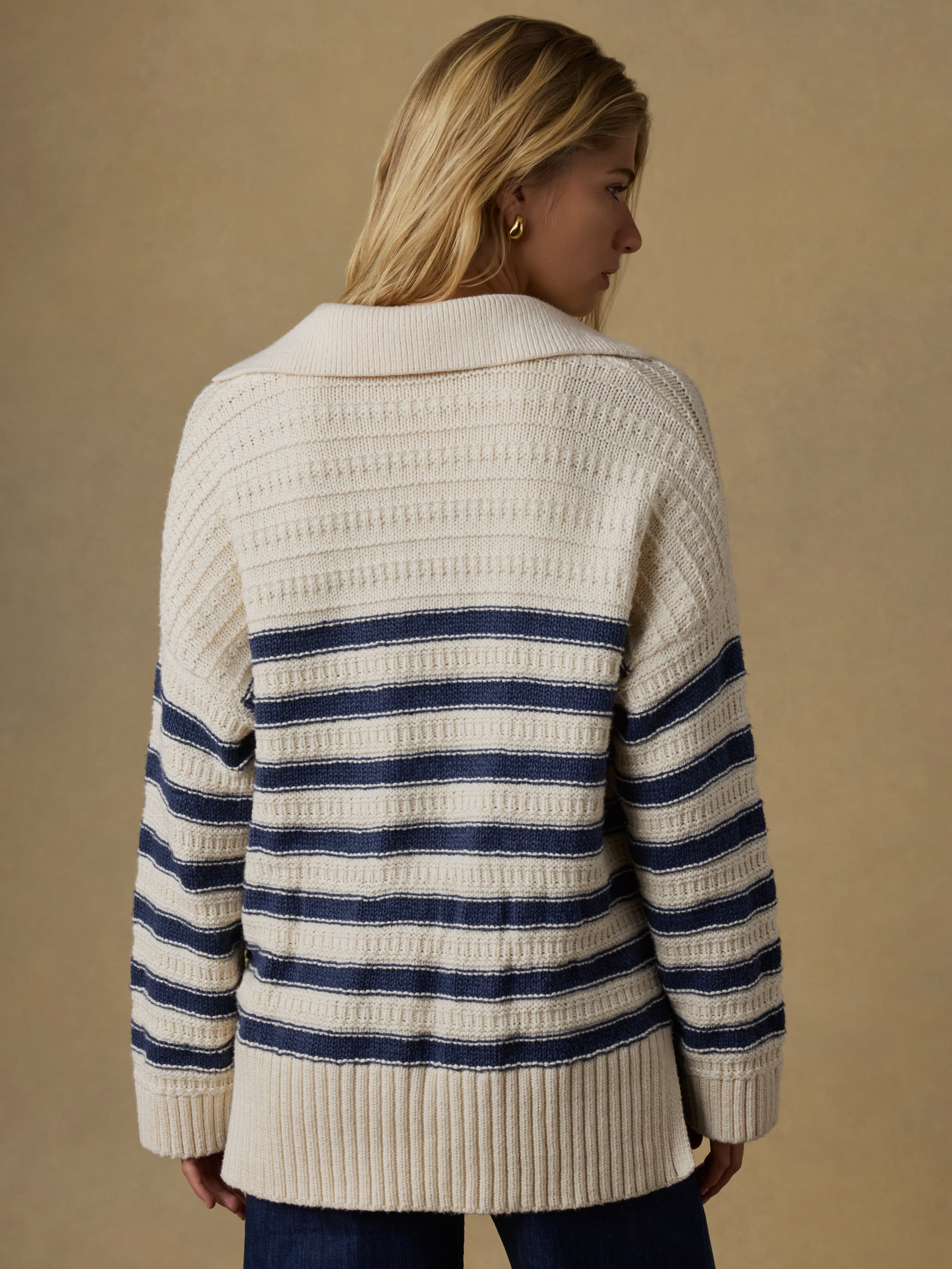 Back view of a woman wearing a white and blue striped sweater with blue jeans against a beige background