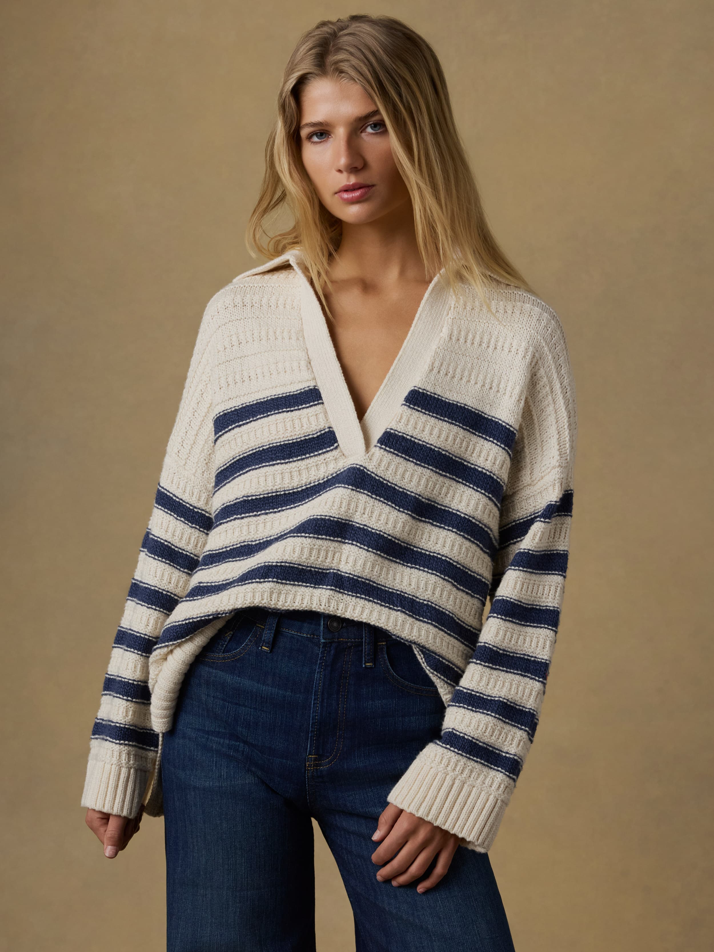 Woman wearing a white and blue striped sweater with blue jeans against a beige background