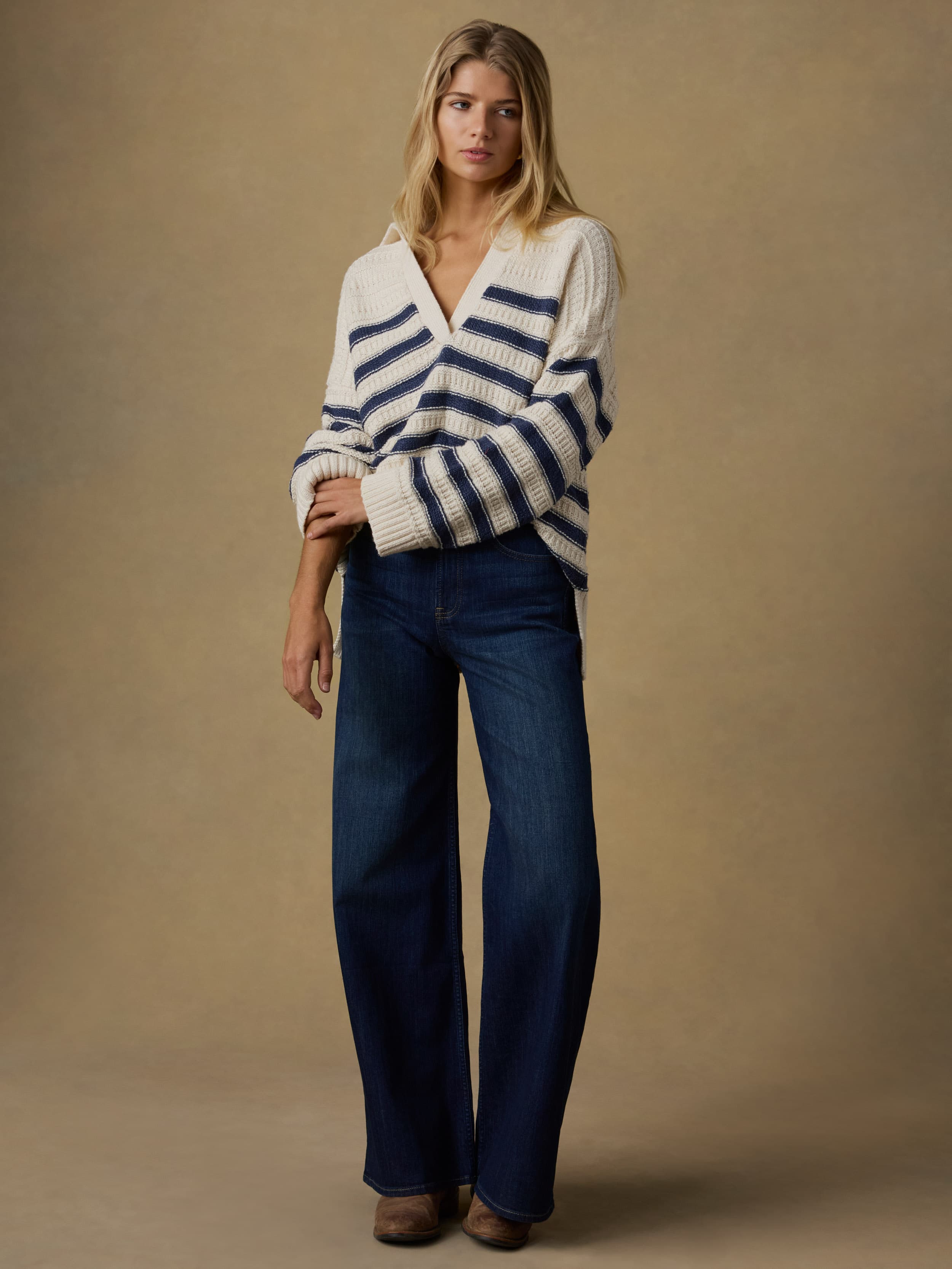 Woman wearing a white and blue striped sweater with blue jeans against a beige background