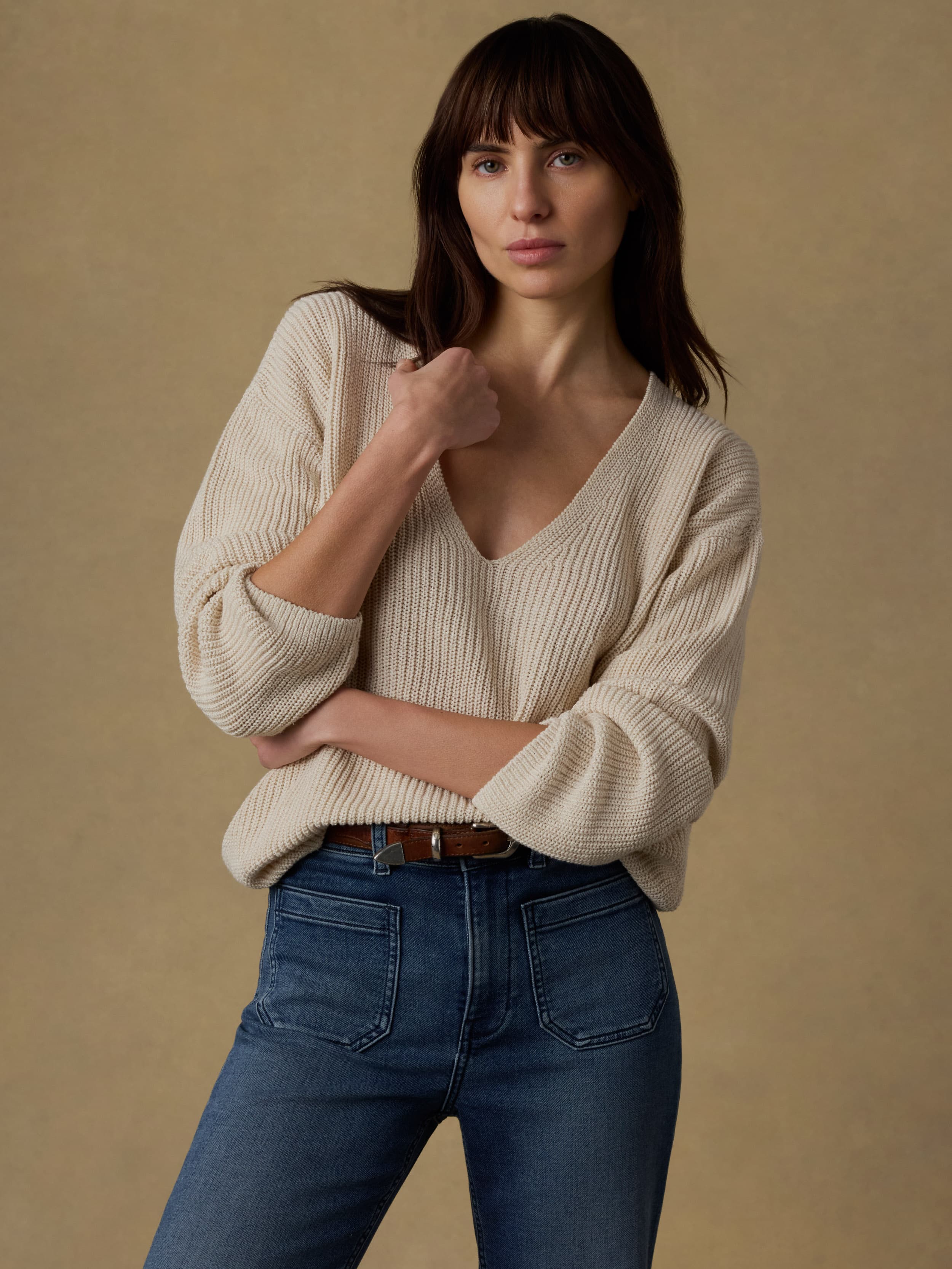 Woman wearing a beige sweater and blue jeans against a beige background