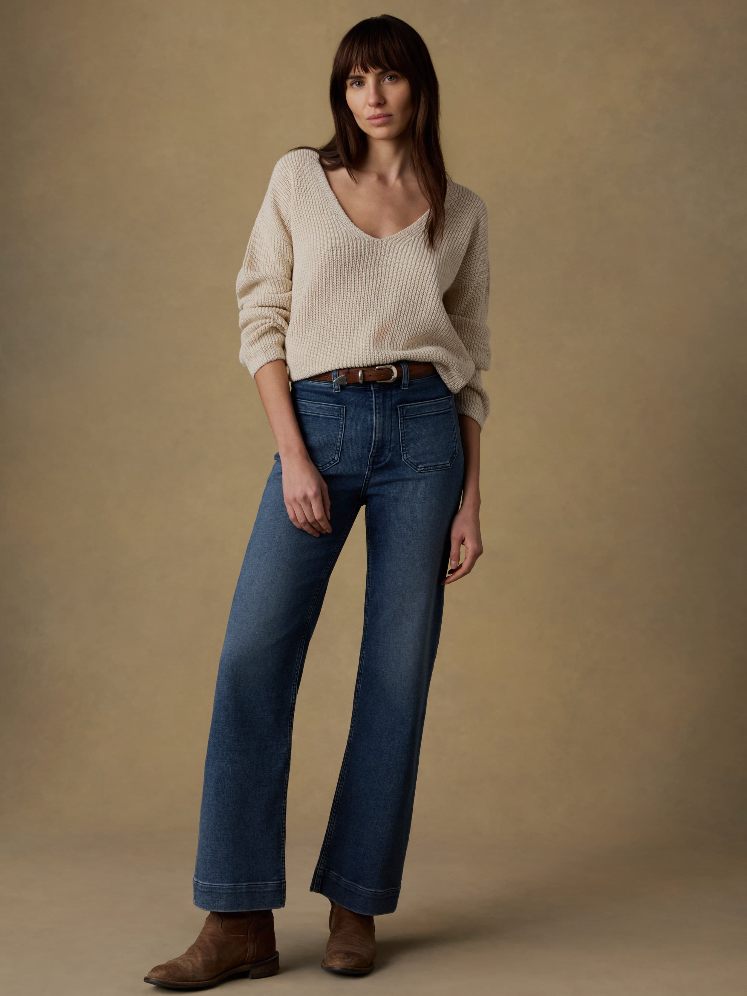Woman wearing a beige sweater and blue jeans against a beige background