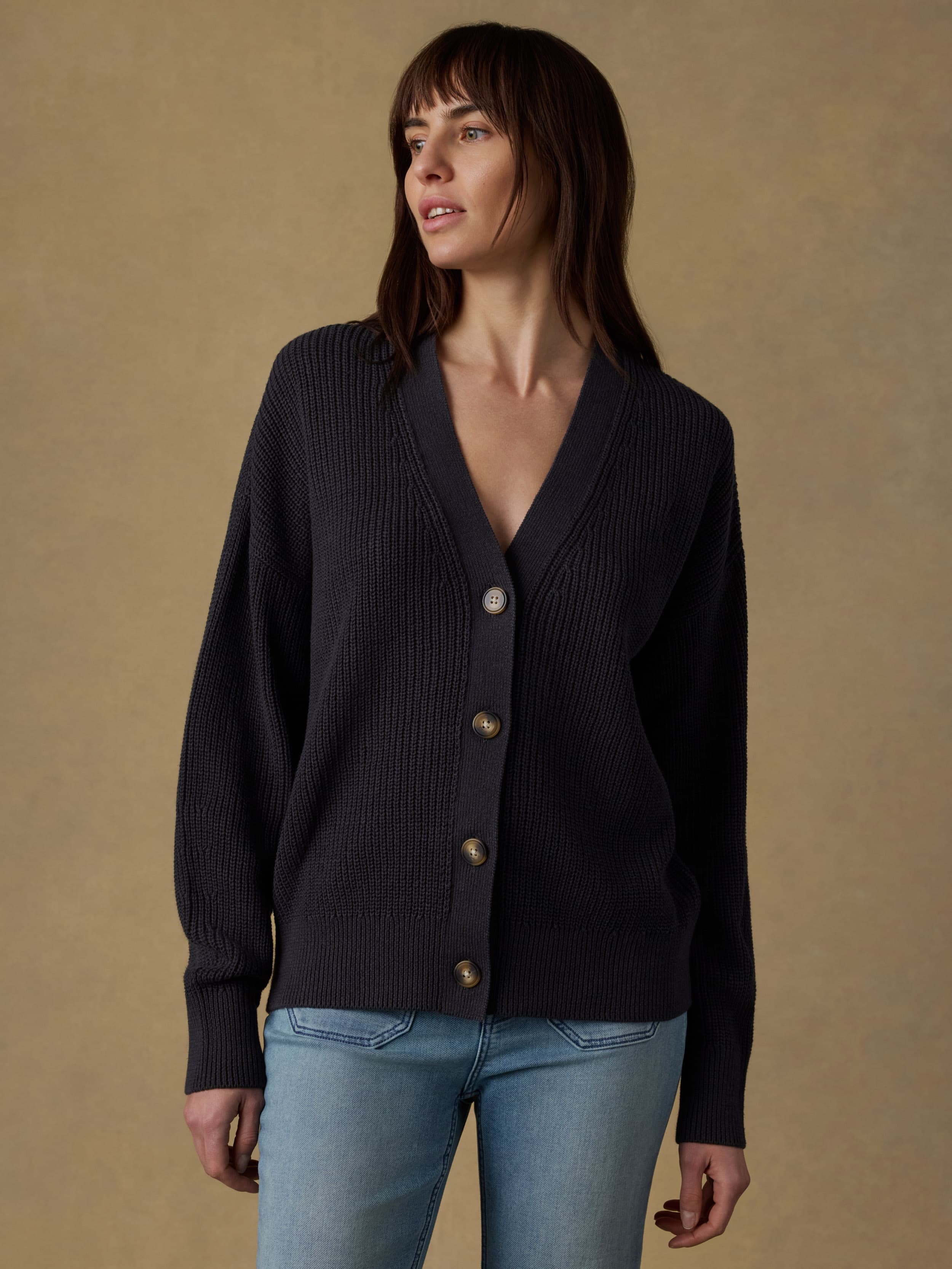 Woman wearing a black knit cardigan and light blue jeans against a beige background