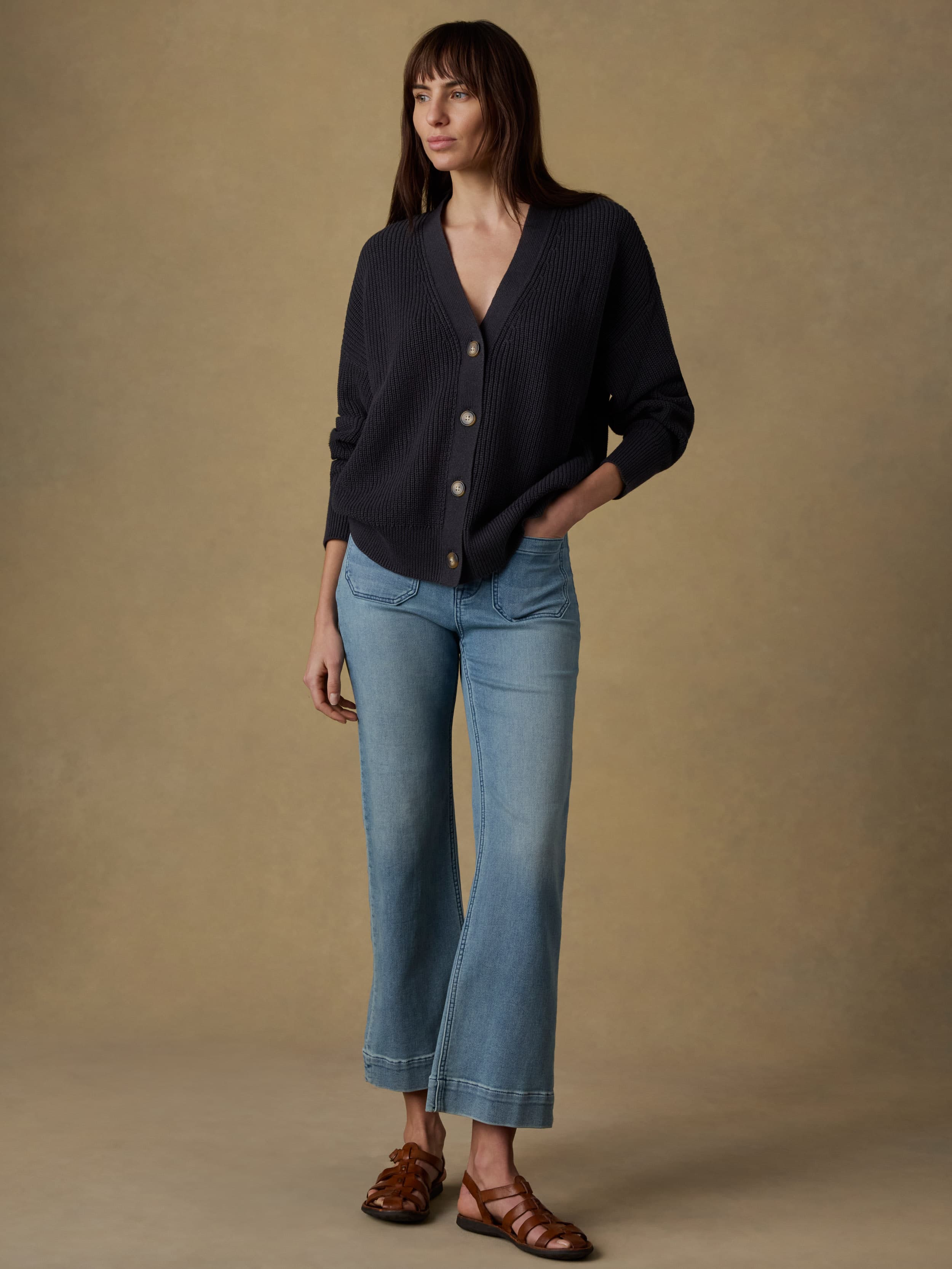 Woman wearing a black knit cardigan and light blue jeans against a beige background