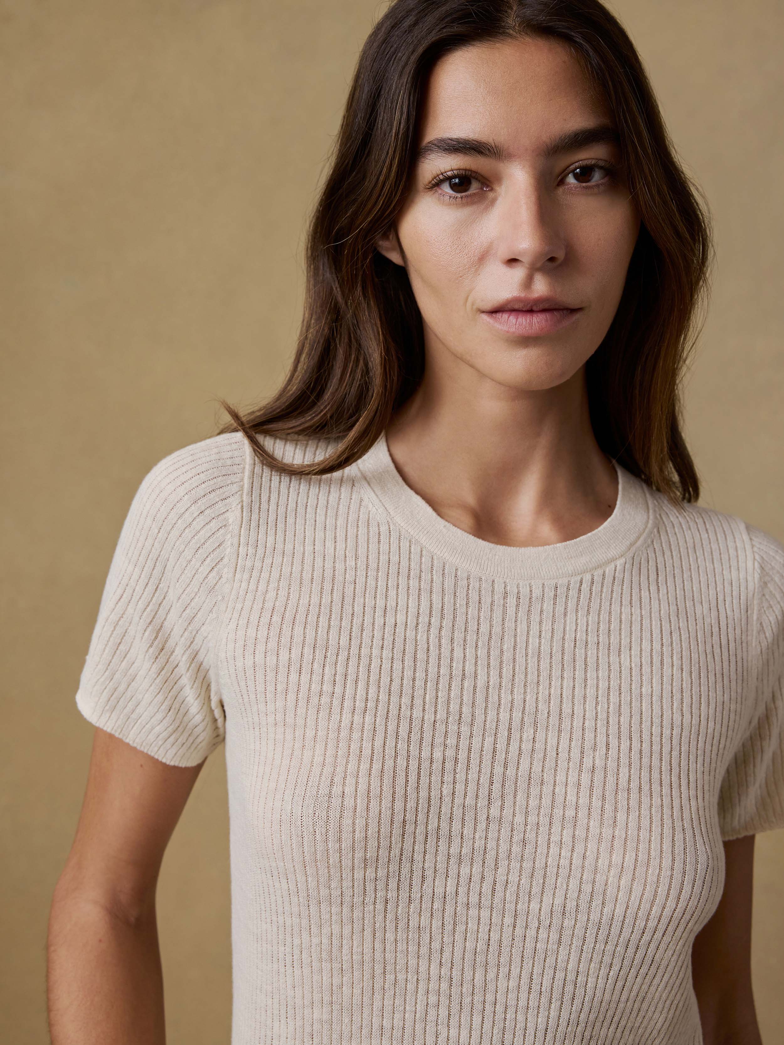 Woman wearing a cream ribbed t-shirt against a beige background