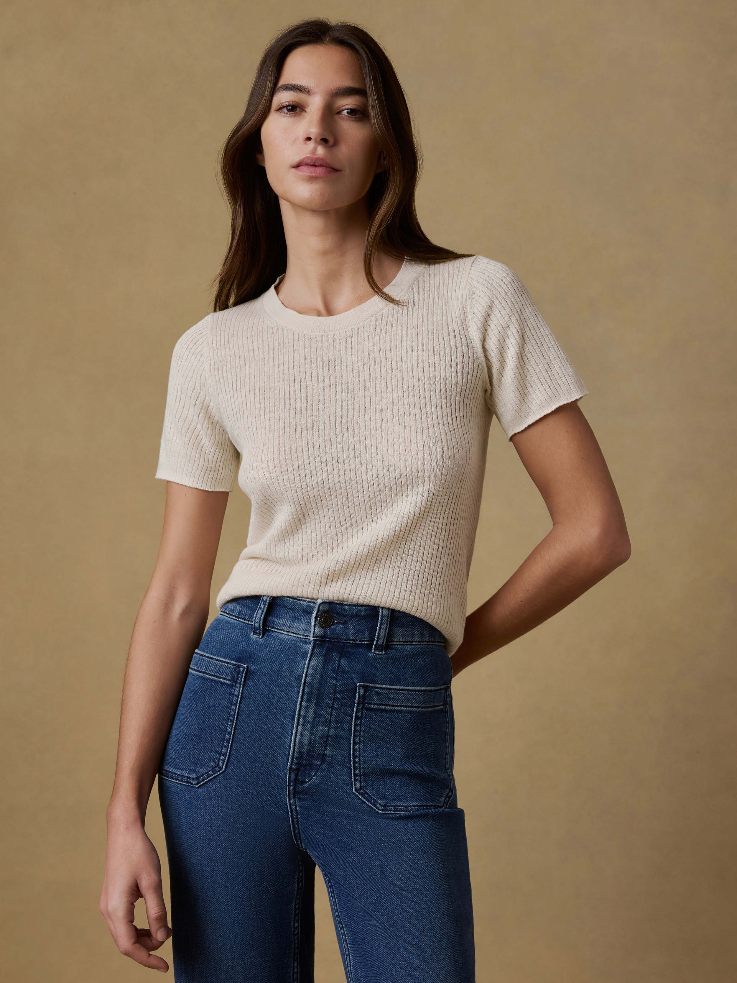 Woman wearing a cream ribbed t-shirt and blue jeans against a beige background