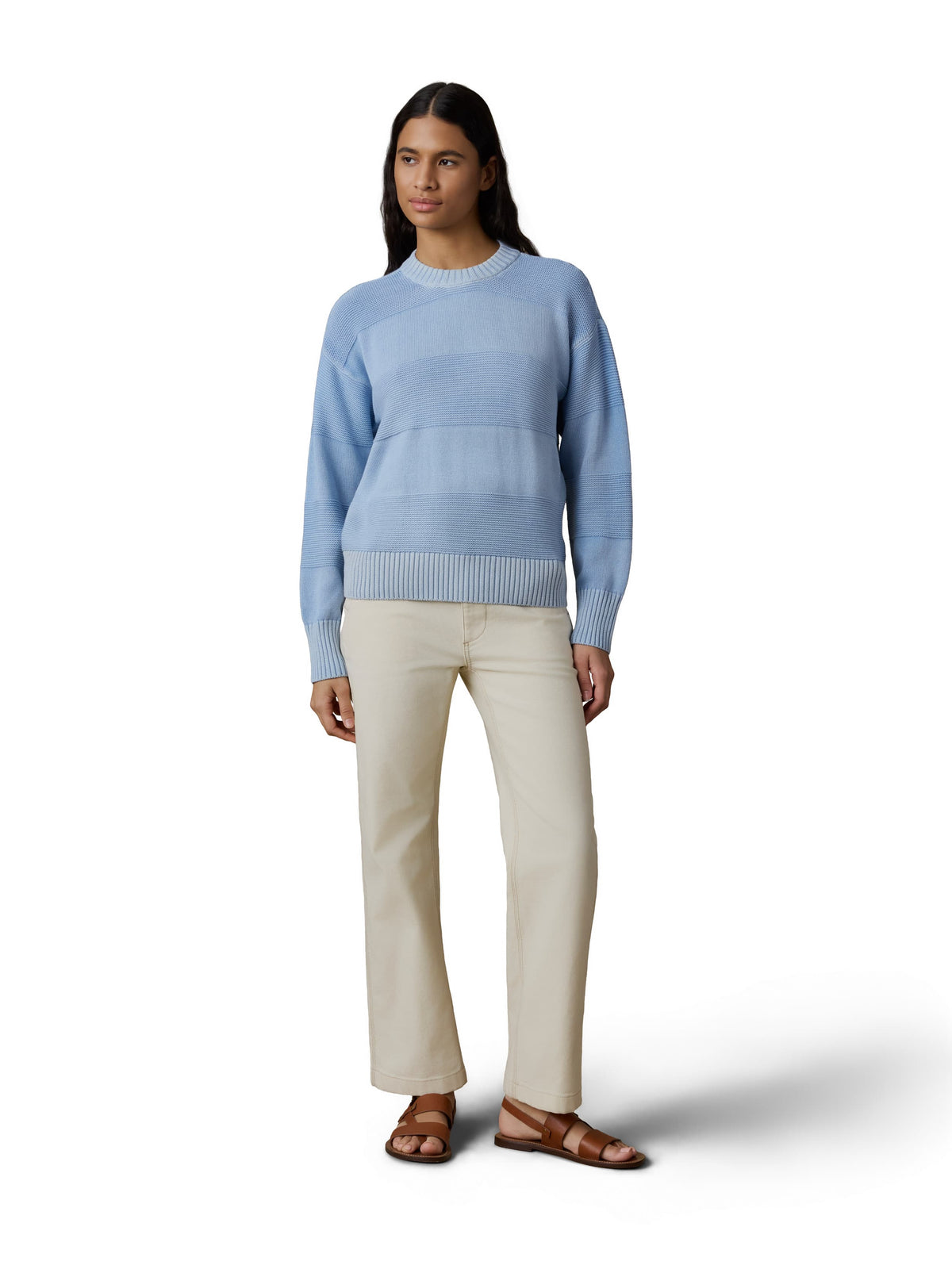 A woman wearing a blue sweater, white pants, and brown sandals, image 2 of 3