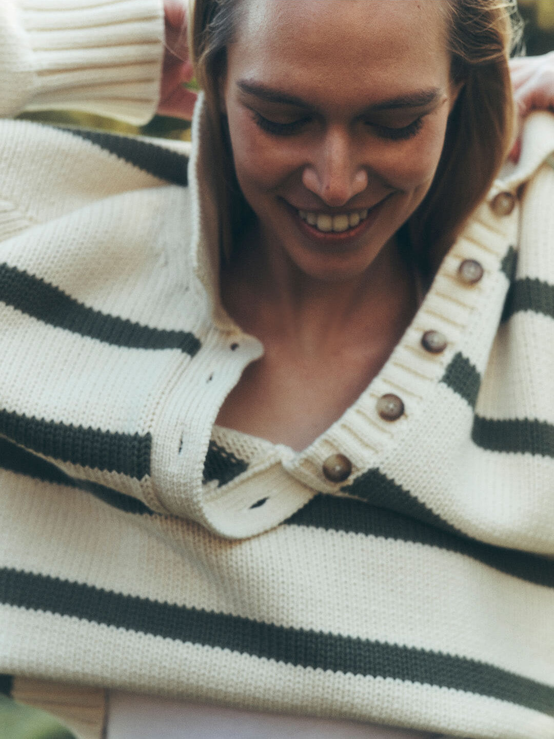 Close up of female model pulling a sunwashed striped sweater over her head