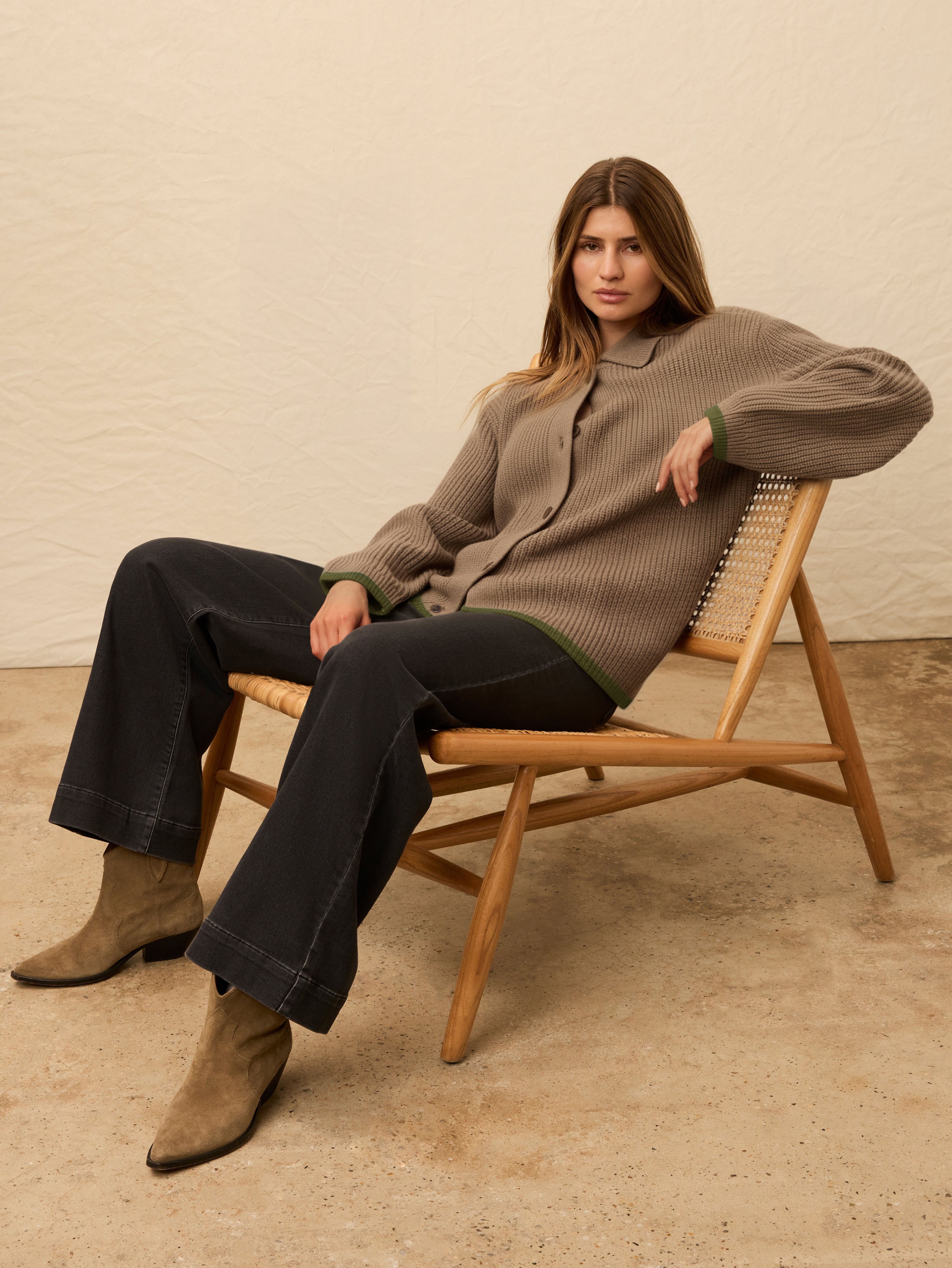 Woman wearing a brown knitted cardigan with black jeans and boots against a beige background