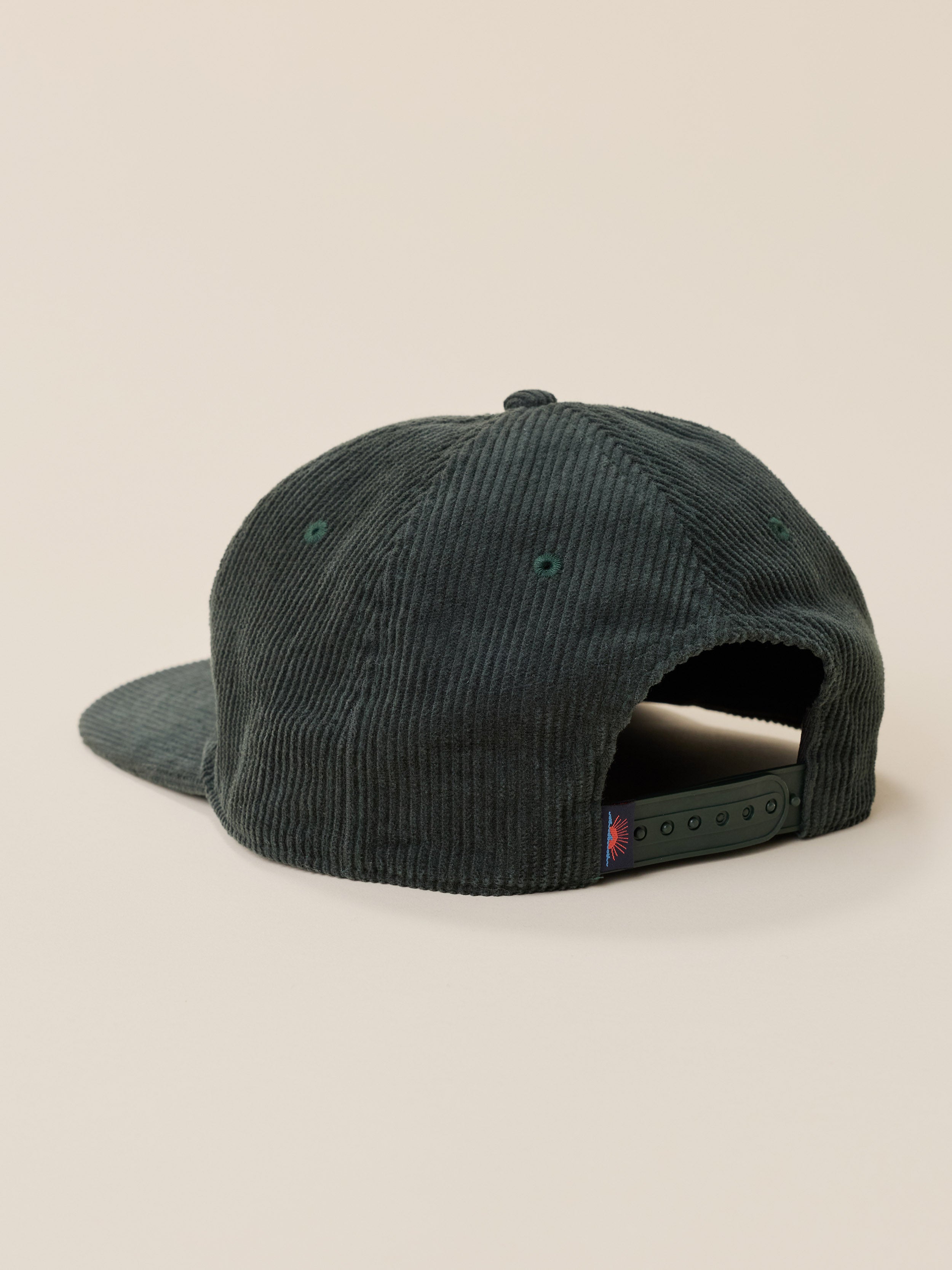 Green corduroy snapback hat against a warm beige studio background