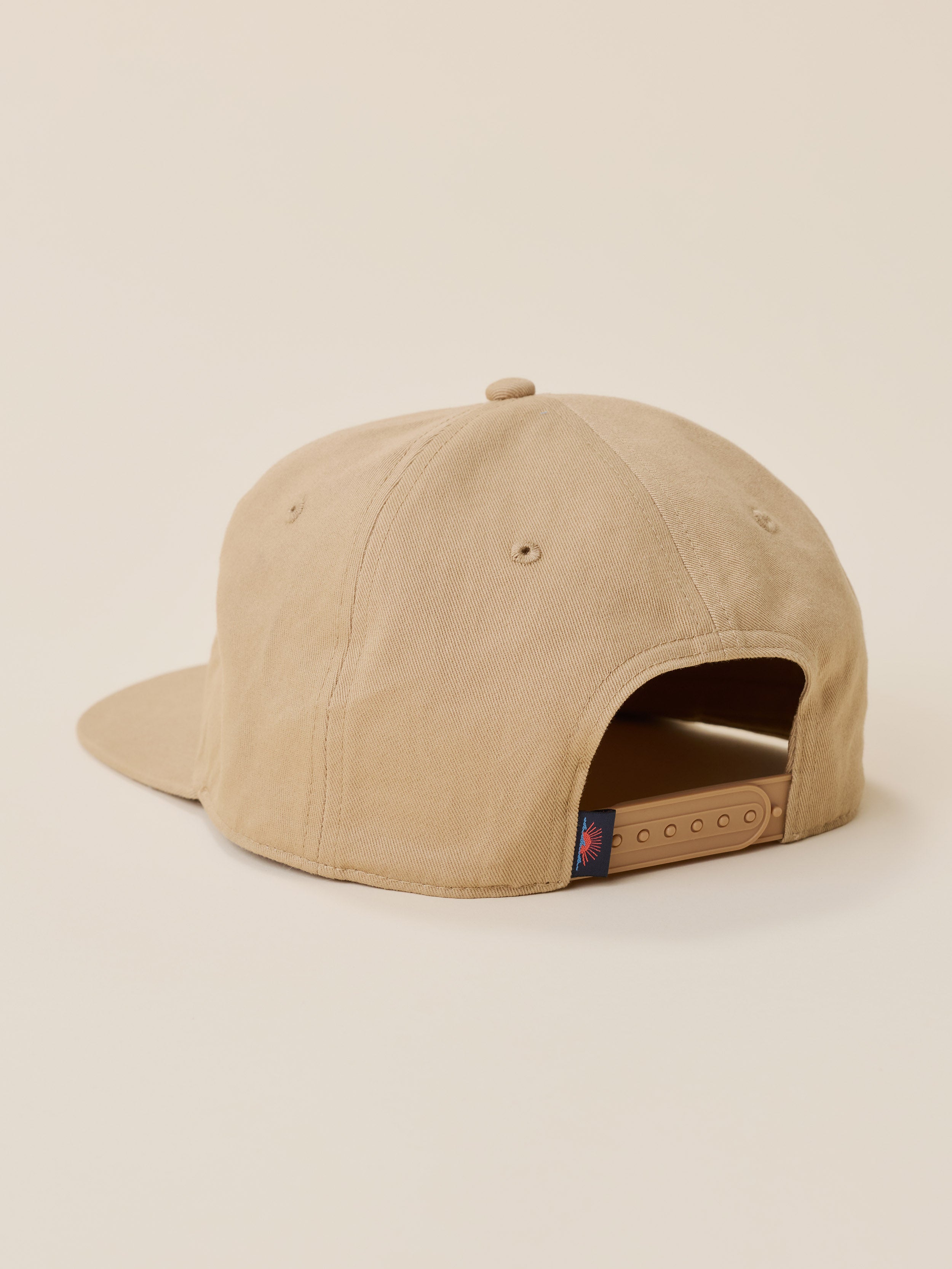 A beige snapback cap shown from the back, featuring a flat brim and an adjustable fabric back closure, photographed against a solid light beige background.