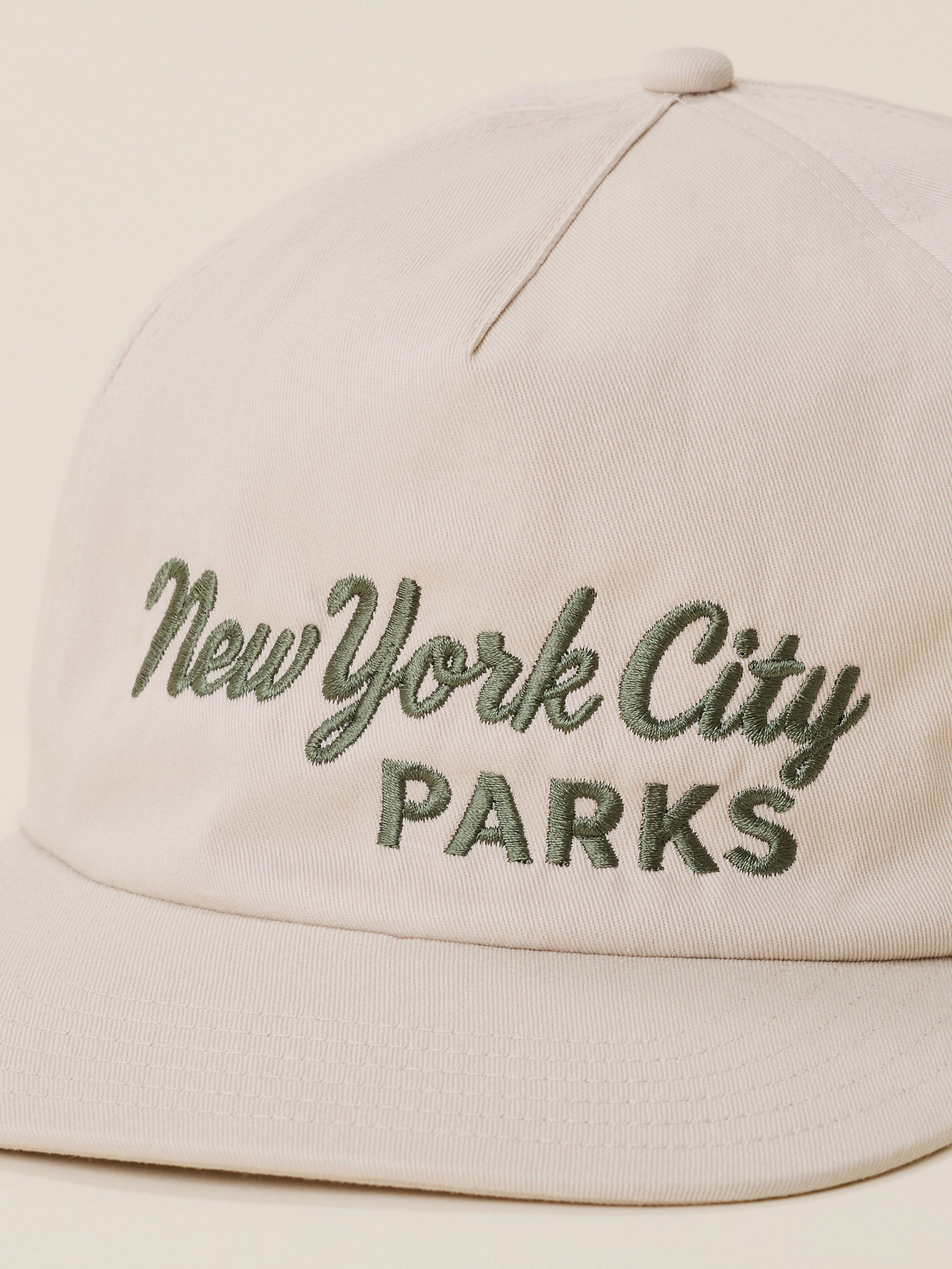 A close-up of a light beige baseball cap featuring 'New York City Parks' embroidered on the front in olive green.