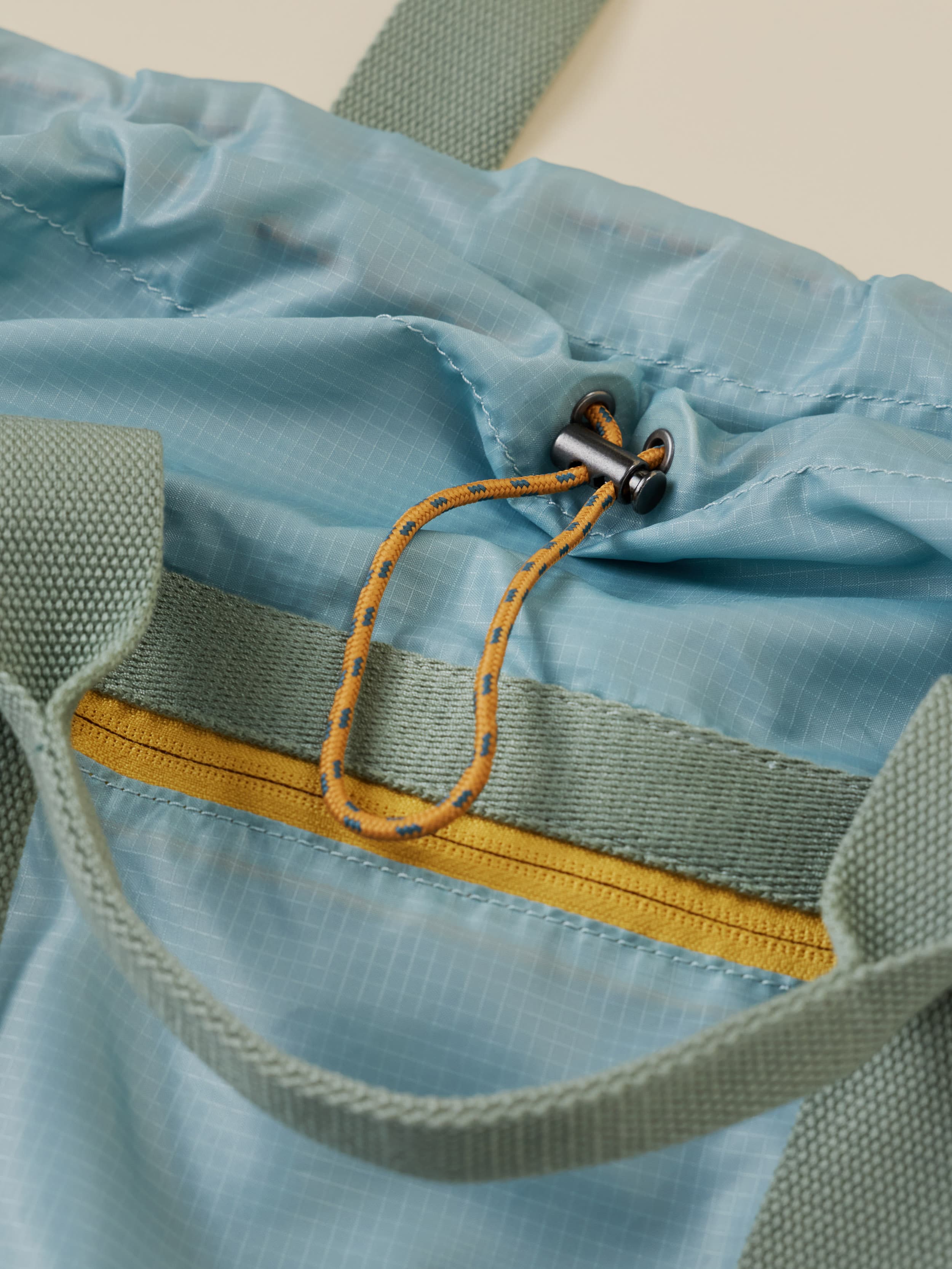 Close-up of a blue bag with a yellow zipper and green straps.