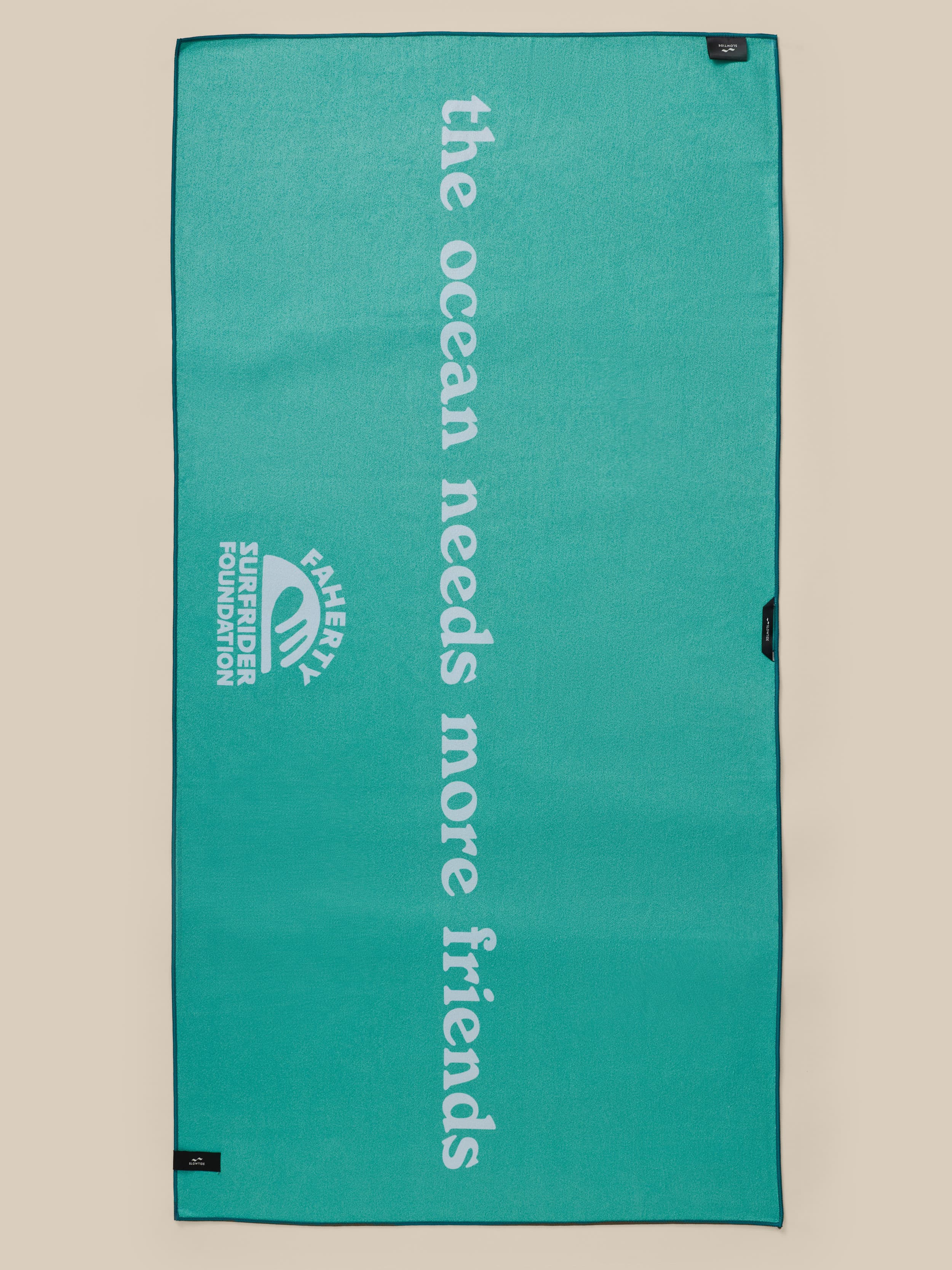 Teal towel with 'the ocean needs more friends' text and Faherty x Surfrider Foundation logo on a beige background