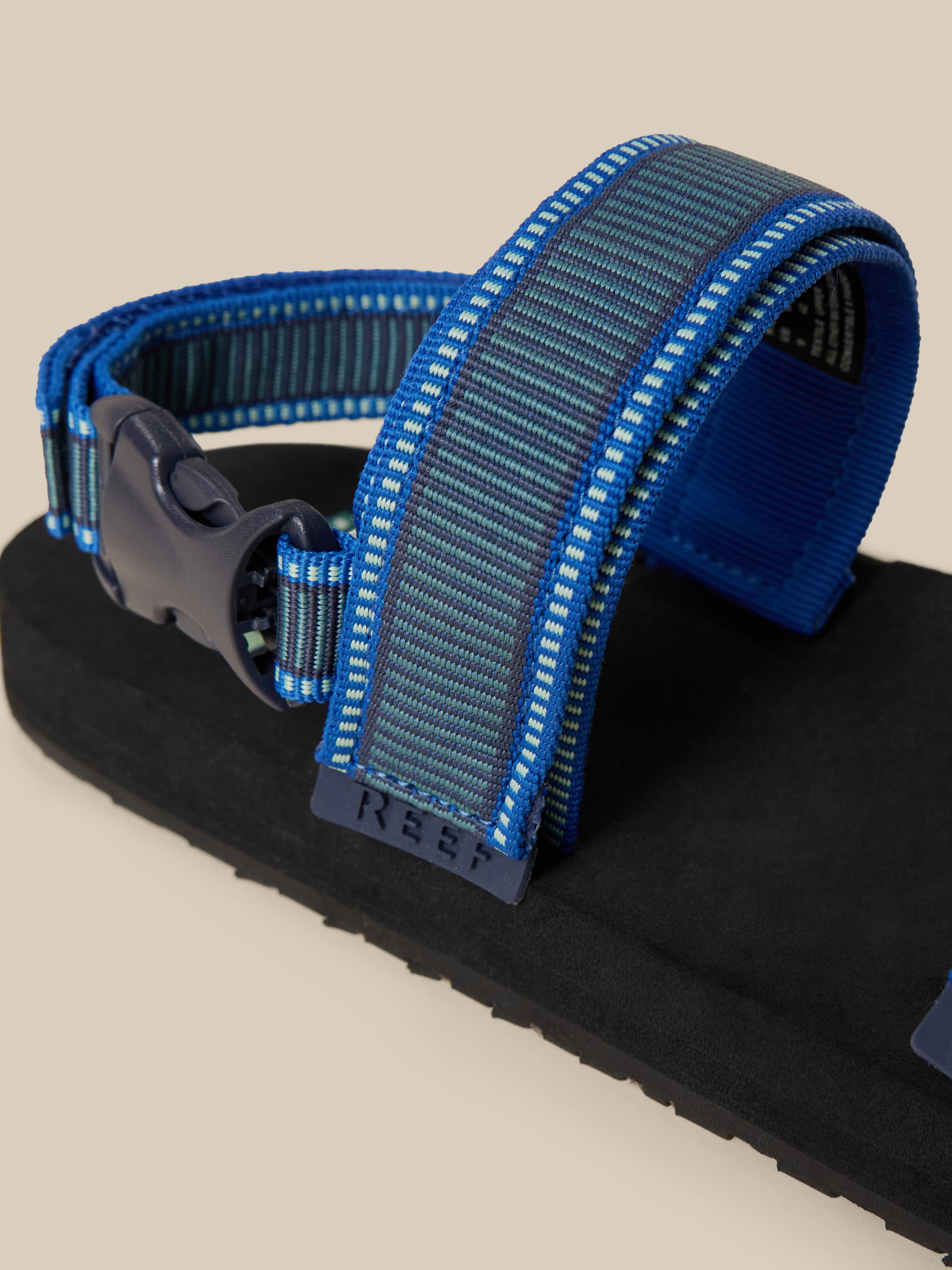 Blue and black sandal with a strap on a beige background