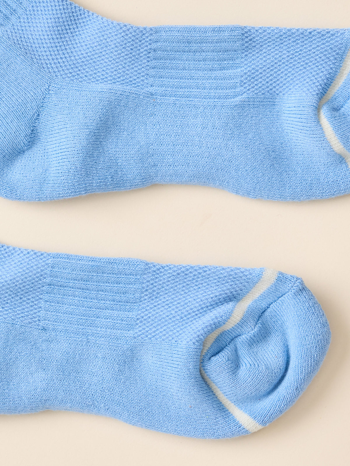 A pair of light blue knit crew socks with white contrast stitching, laid flat on a warm beige background.