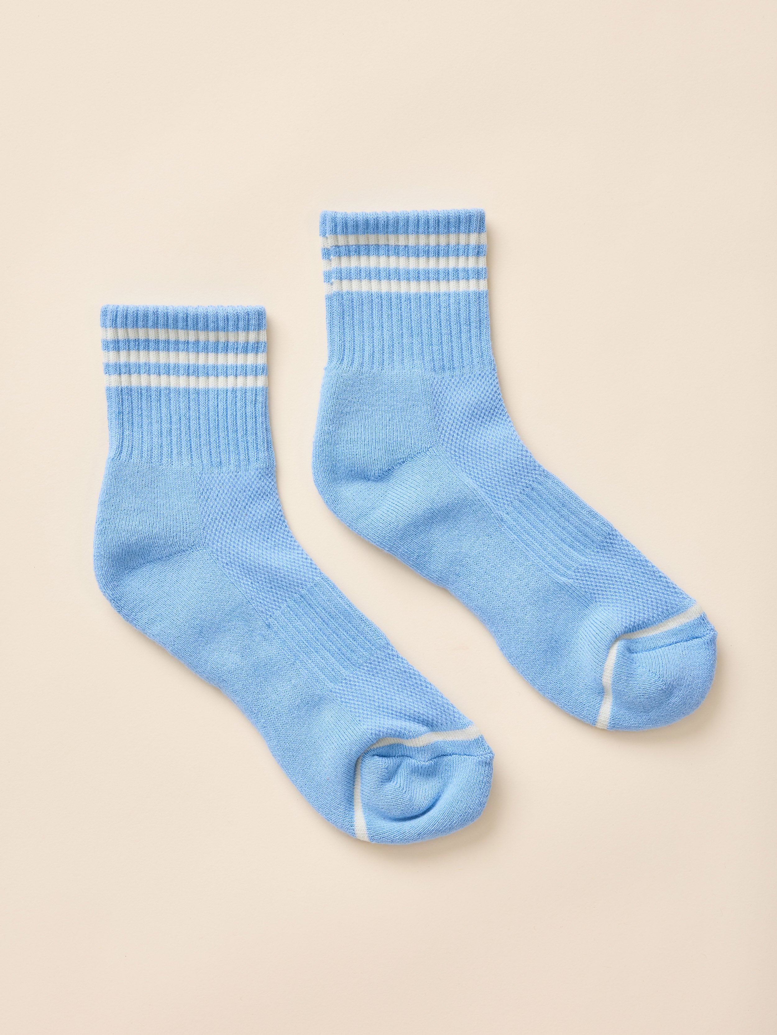 A pair of light blue knit crew socks with white contrast stitching, laid flat on a warm beige background.