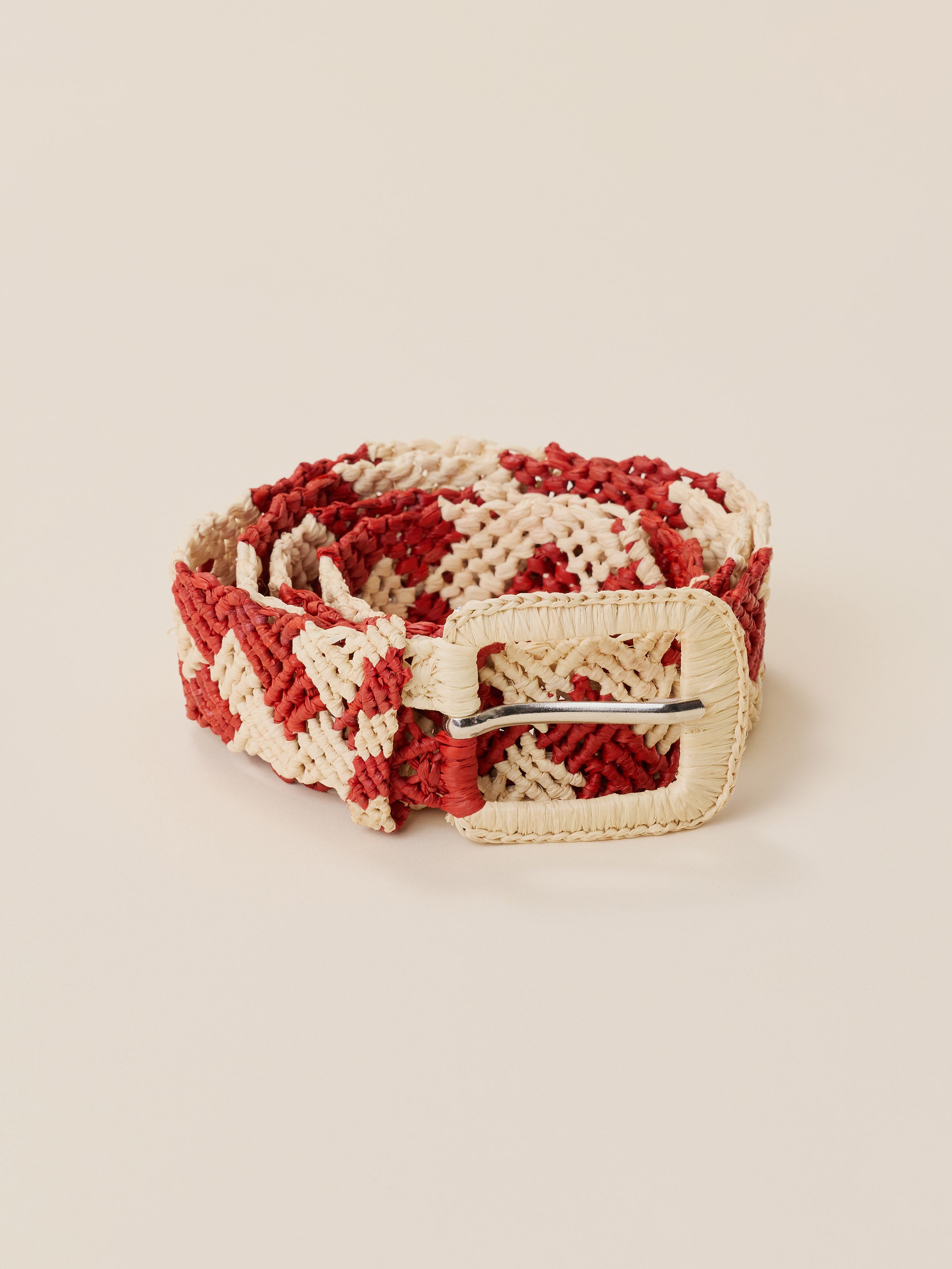 A woven belt with a red and cream chevron pattern and a cream buckle, displayed on a solid beige background.